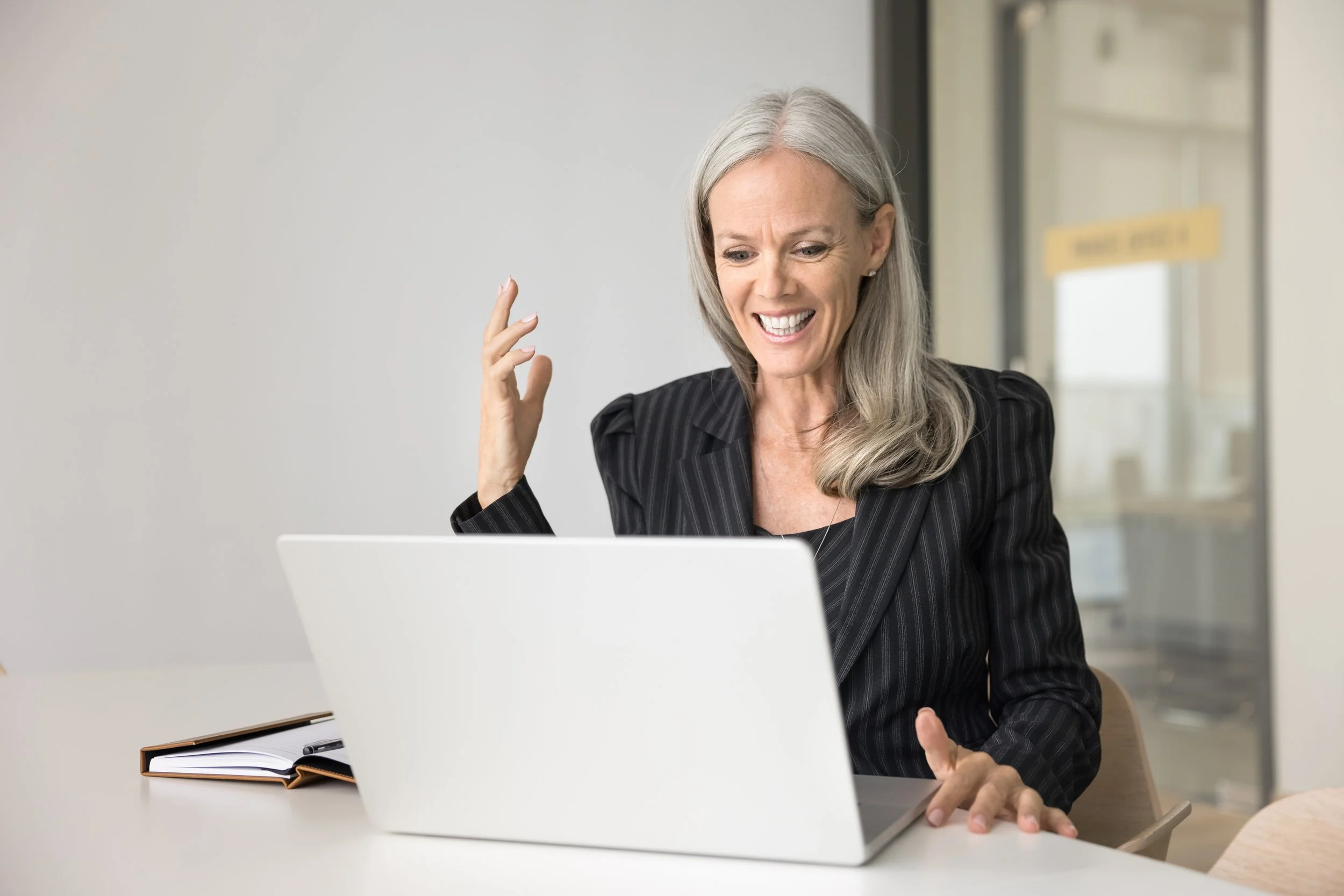 A smiling female senior executive with gray hair looking at a computer screen in an office setting.