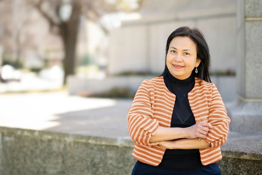 Mary Vaz, career transition coach in Australia, wearing a black top and an orange striped blazer, standing outdoors with her arms crossed, smiling at the camera.