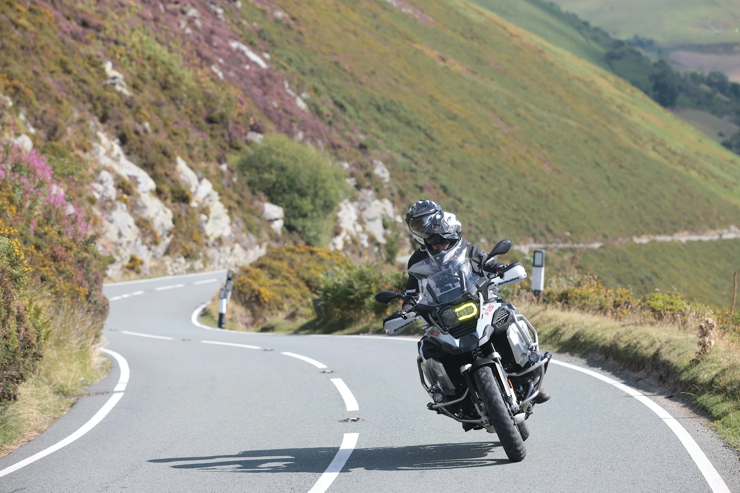 A person riding a motorcycle on a winding mountain road surrounded by greenery and hills.