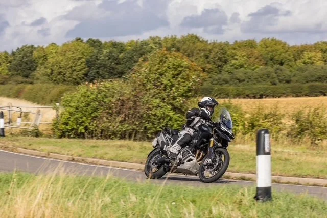 Motorcyclist riding a black motorcycle on a rural road surrounded by field and trees.