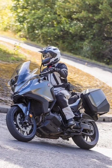 Person riding a black motorcycle with a helmet, on a road with trees in the background.