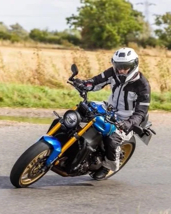 Motorcyclist riding a blue sport bike on a rural road, wearing a white helmet and black riding gear.