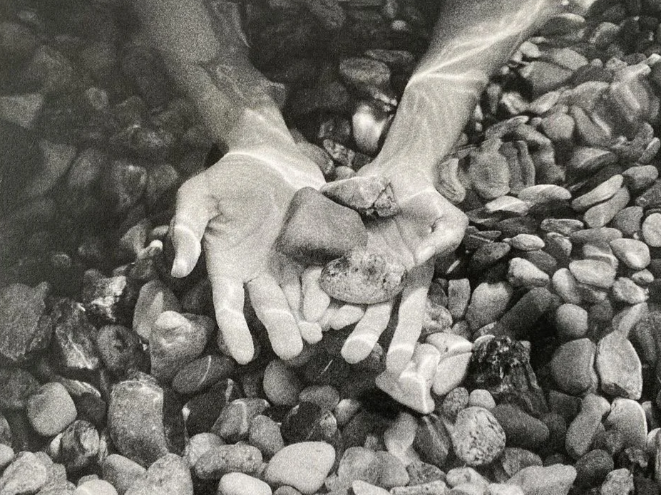 Two hands gently holding a small rock among numerous pebbles and stones.