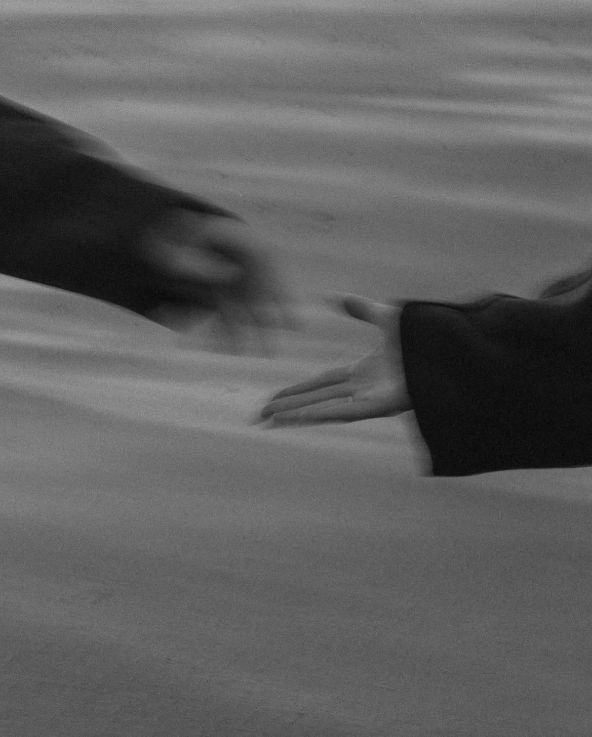 Black and white photo of two hands gently touching or holding on a surface.