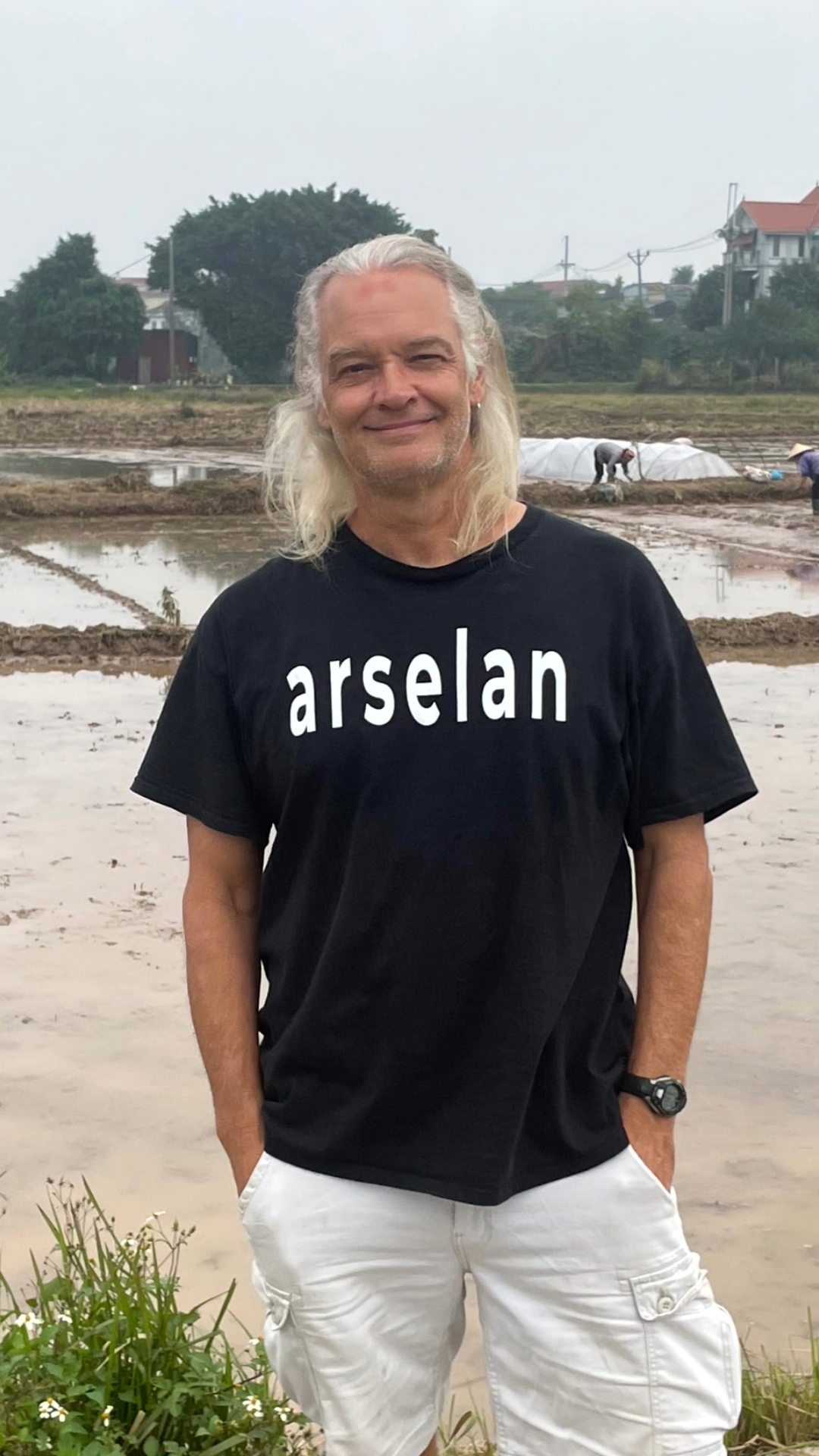 Author and Traveler JT Shull wearing an Arselan t-shirt and standing next to a rice paddy
