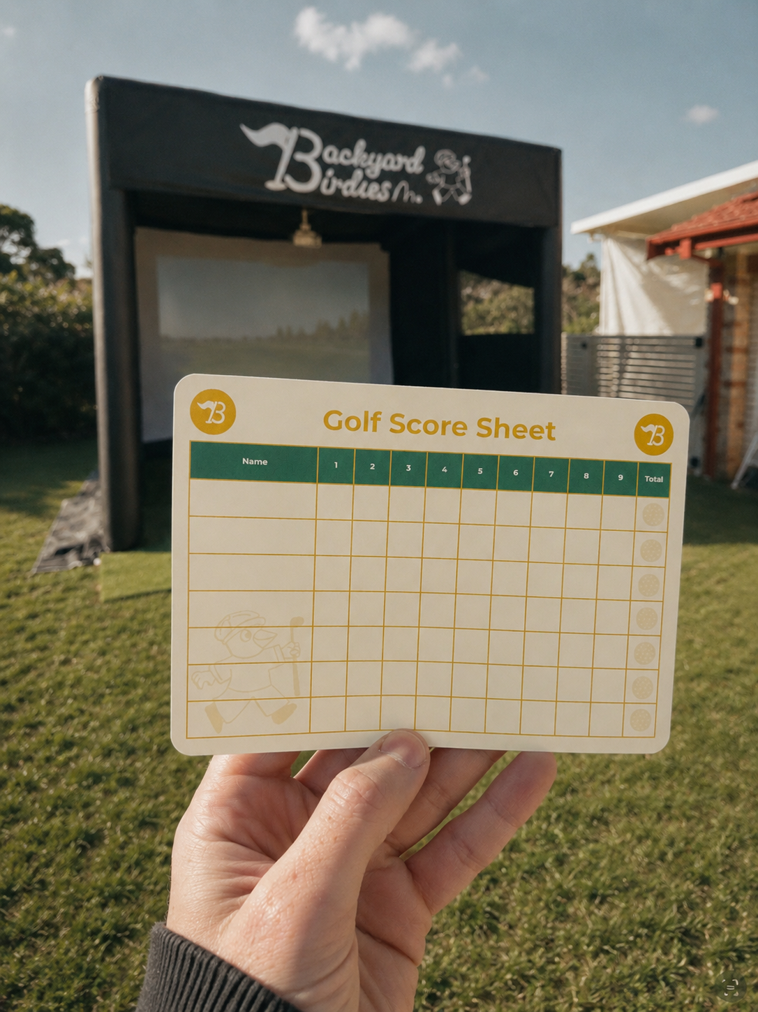 Hand holding a golf score sheet in front of a blackboard with 'Backyard Birdies' written on it, on a grassy outdoor area under a blue sky.