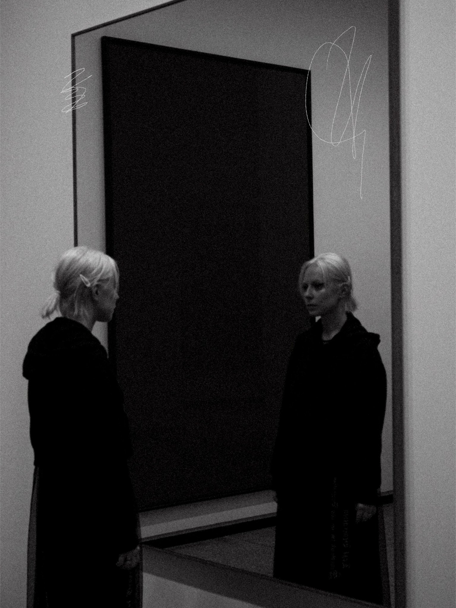 Women with blonde hair in black clothing standing in front of a large mirror in a  New National gallery Berlin.