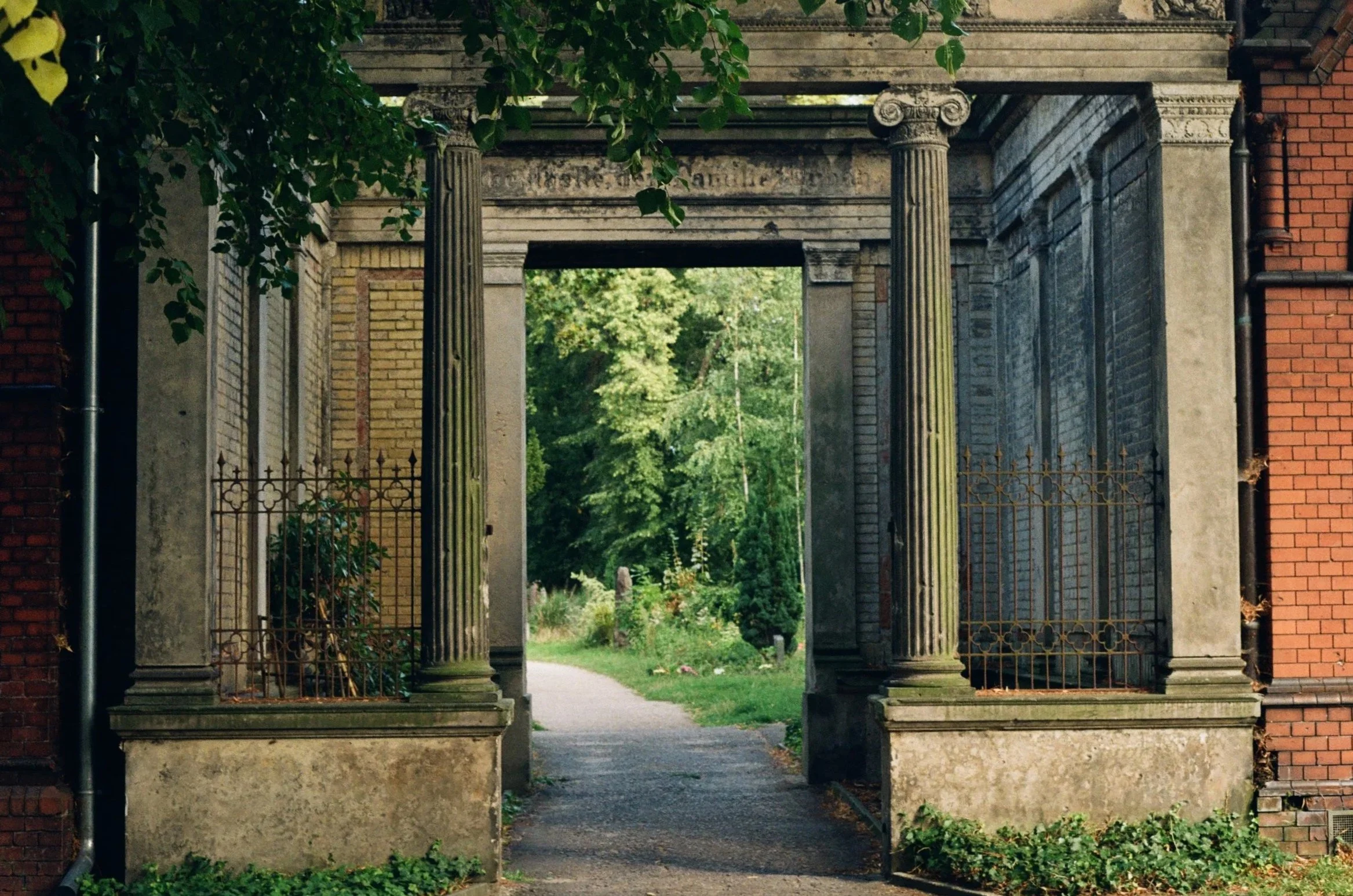 Historic cemetery monument with classical columns, carved ornamentation and overgrown ivy at Friedhöfe an der Bergmannstraße in Berlin.