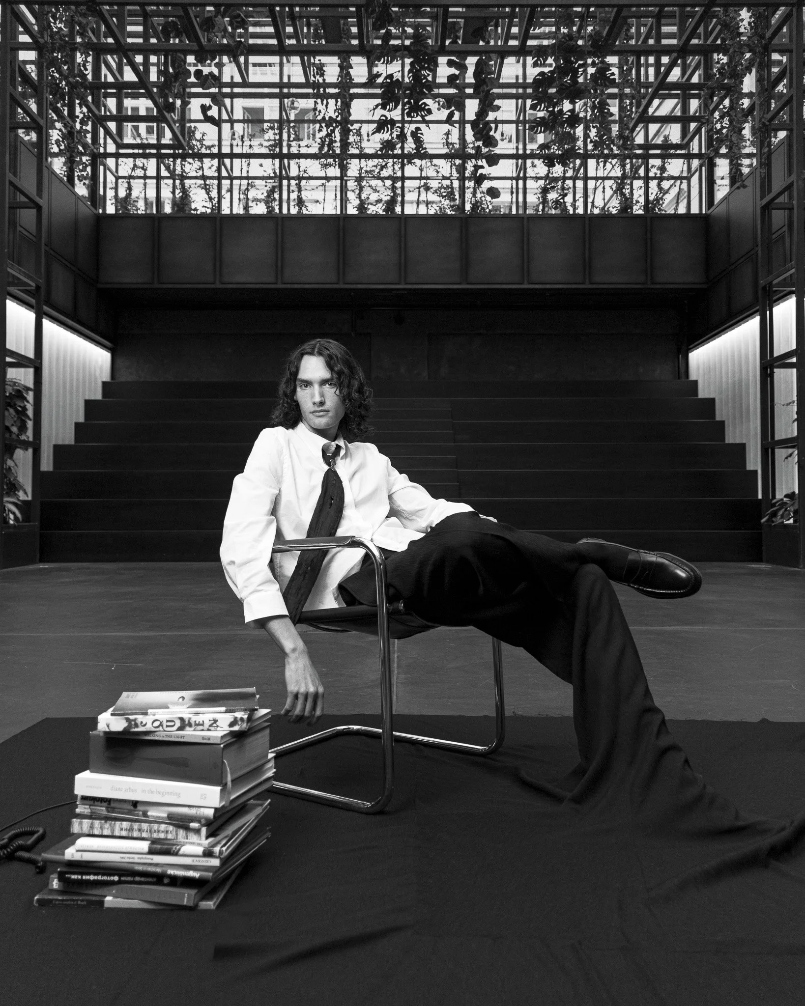 Black and white photograph of a seated person in a modern interior, surrounded by geometric shadows and architectural lines.