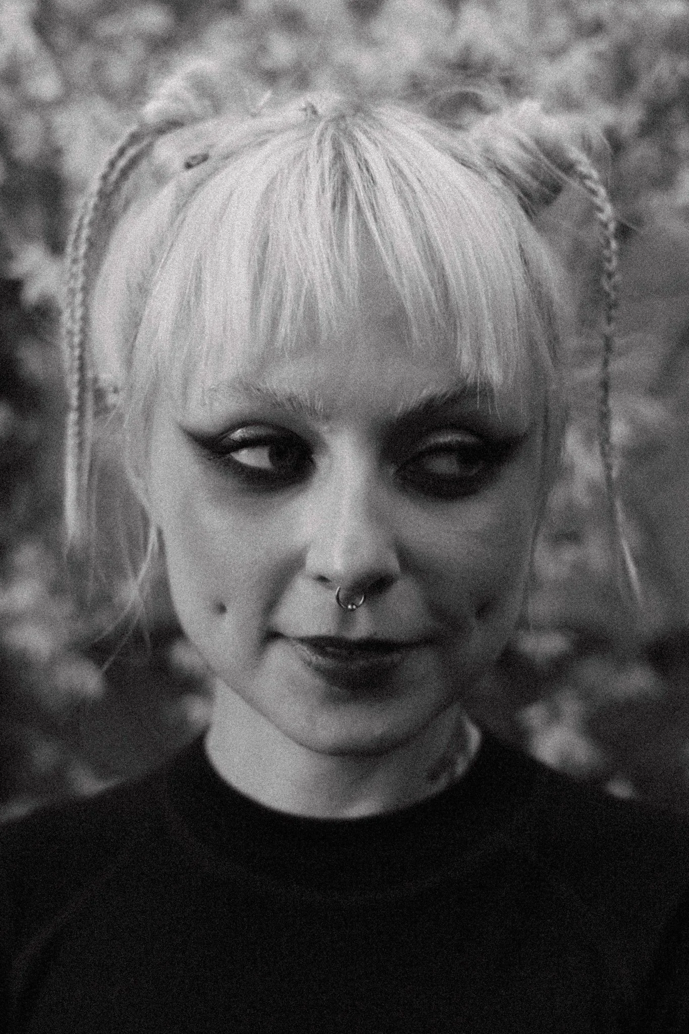 Black and white close-up photo of a woman with light-colored hair, makeup, and facial piercings.