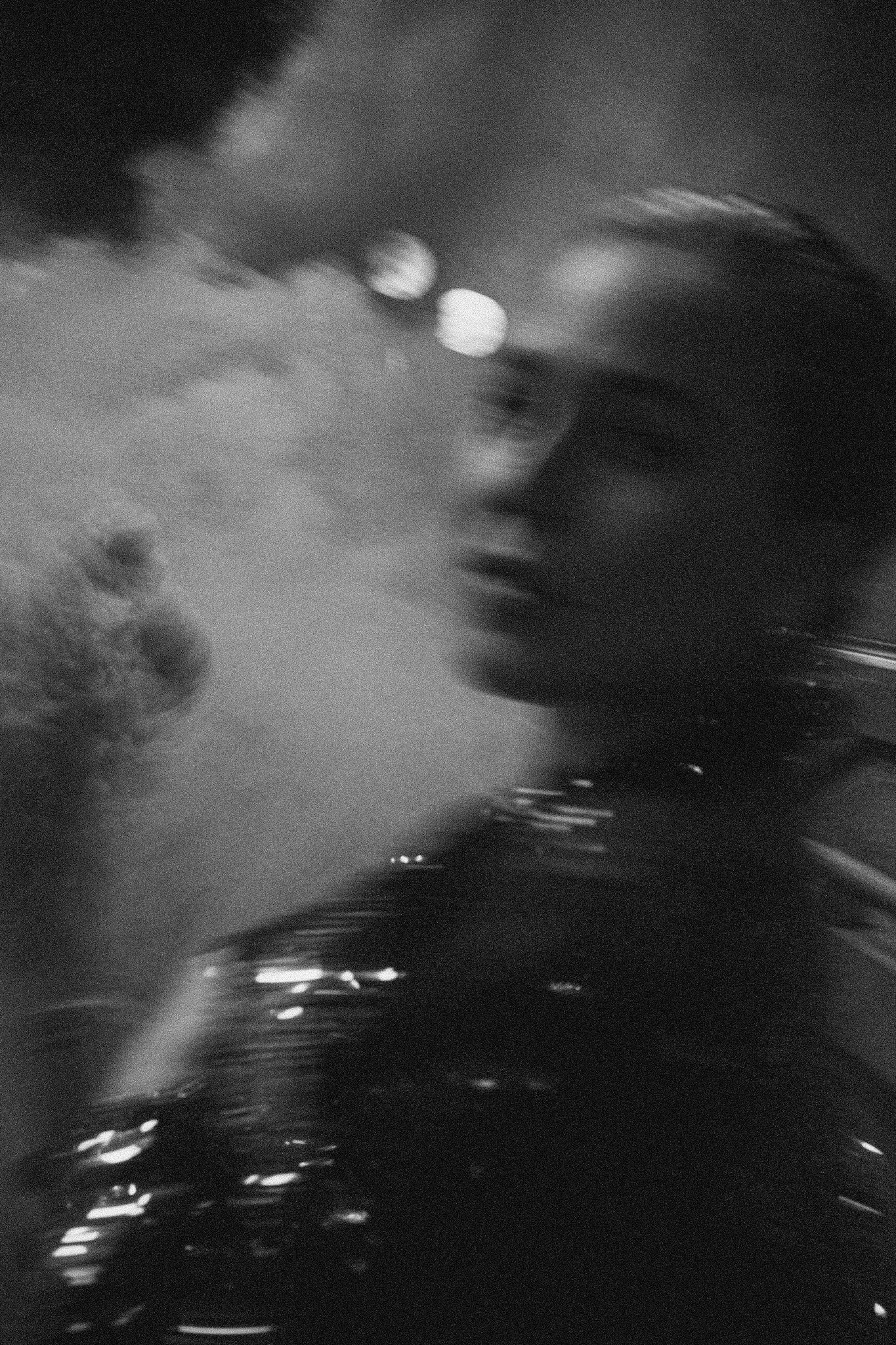 Blurred black and white portrait of a woman surrounded by smoke and soft city lights at night.