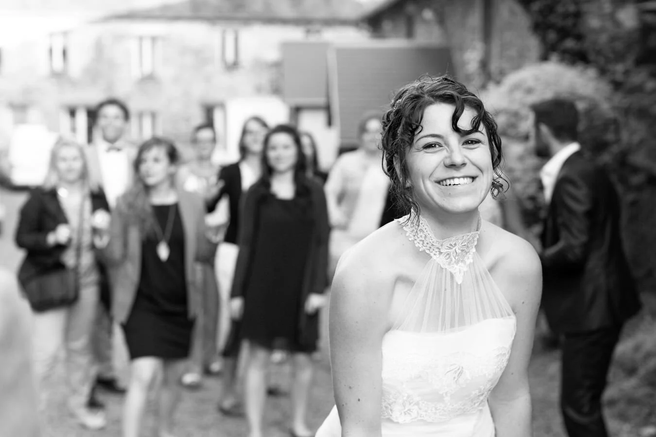 Une femme souriante en robe de mariage devant un groupe de personnes lors d'un mariage en plein air.