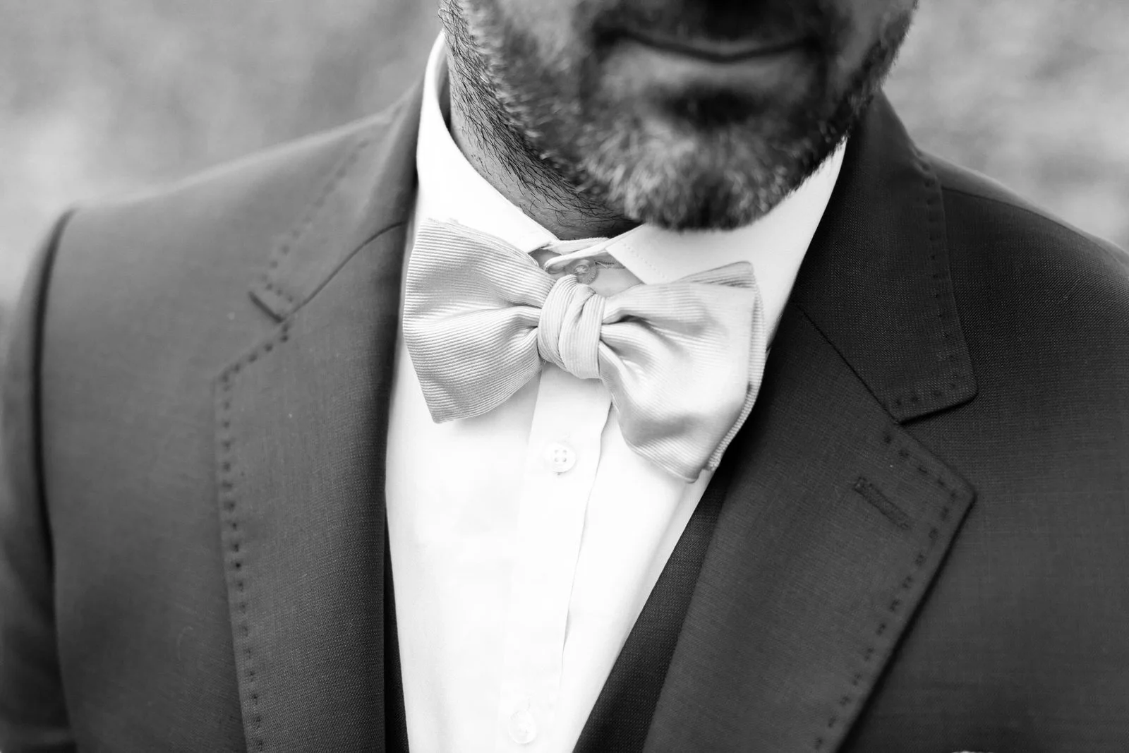 Homme en costume avec nœud papillon blanc, vu de près dans une photo en noir et blanc.