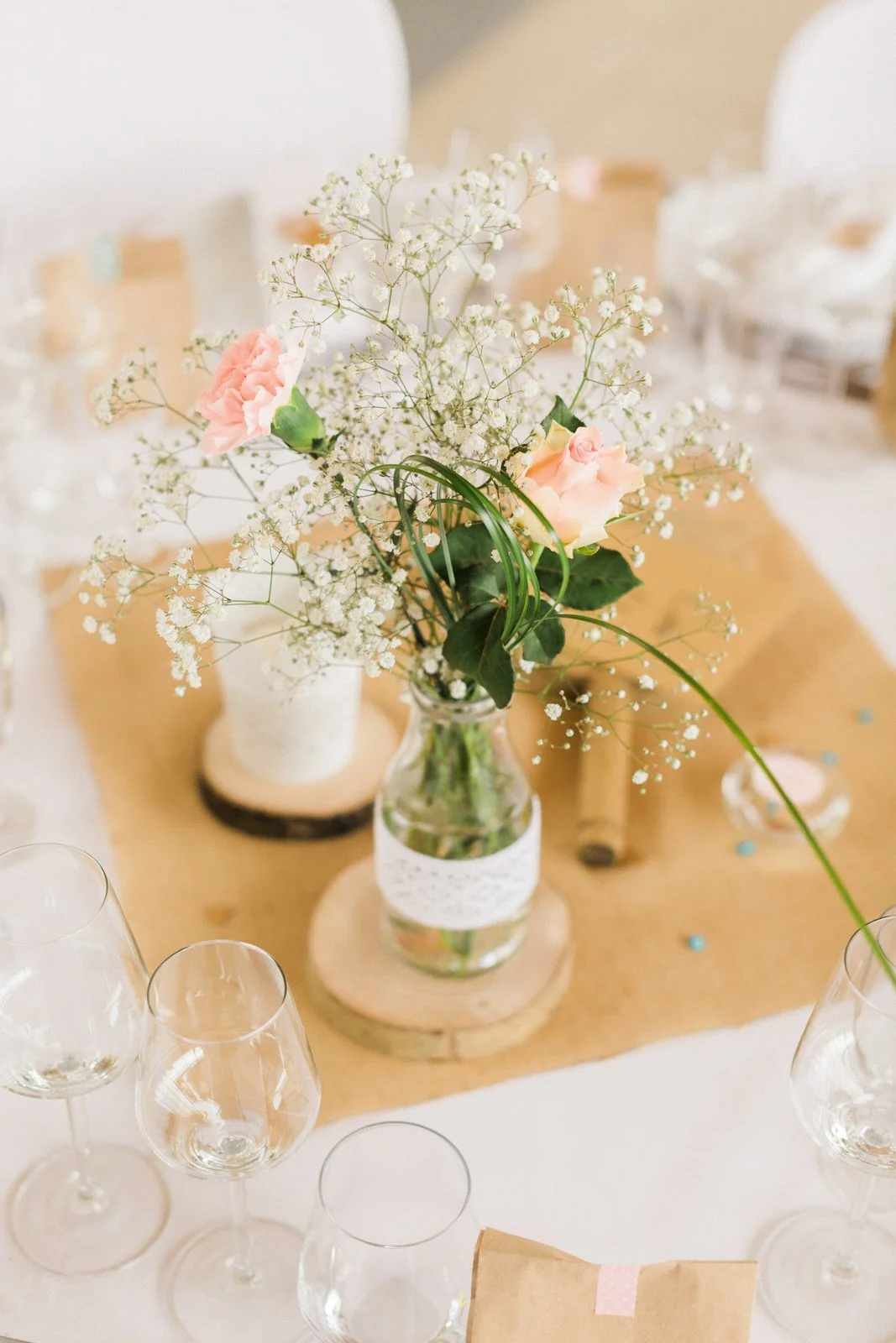 Centre de table floral avec des roses roses, des oeillets blancs et de la gypsophile dans un vase en verre sur une table de fête.