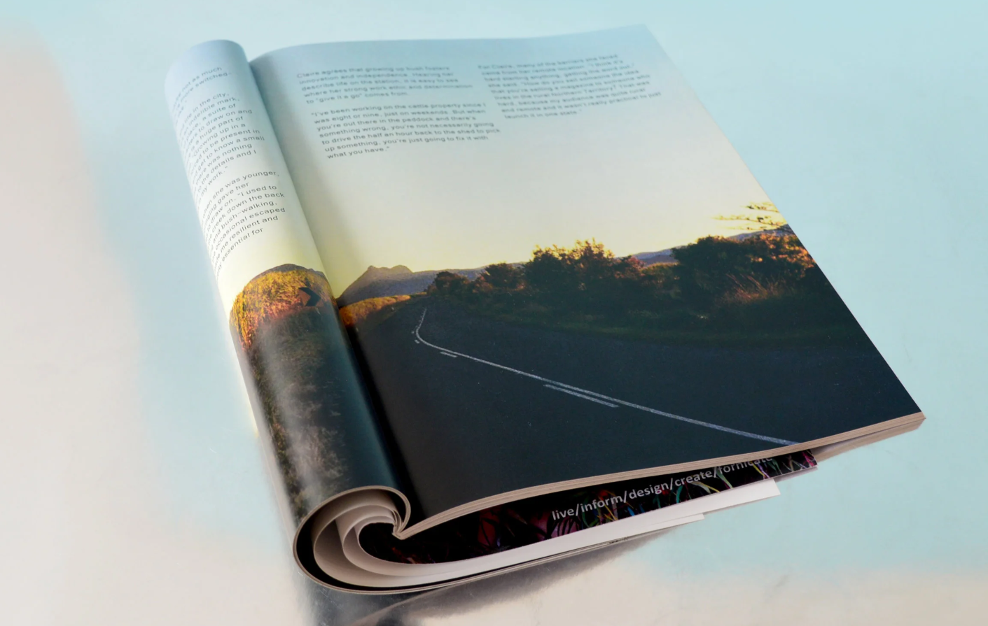 Open magazine displaying a landscape photograph of a curving road, vegetation, and a mountain in the distance at sunset.