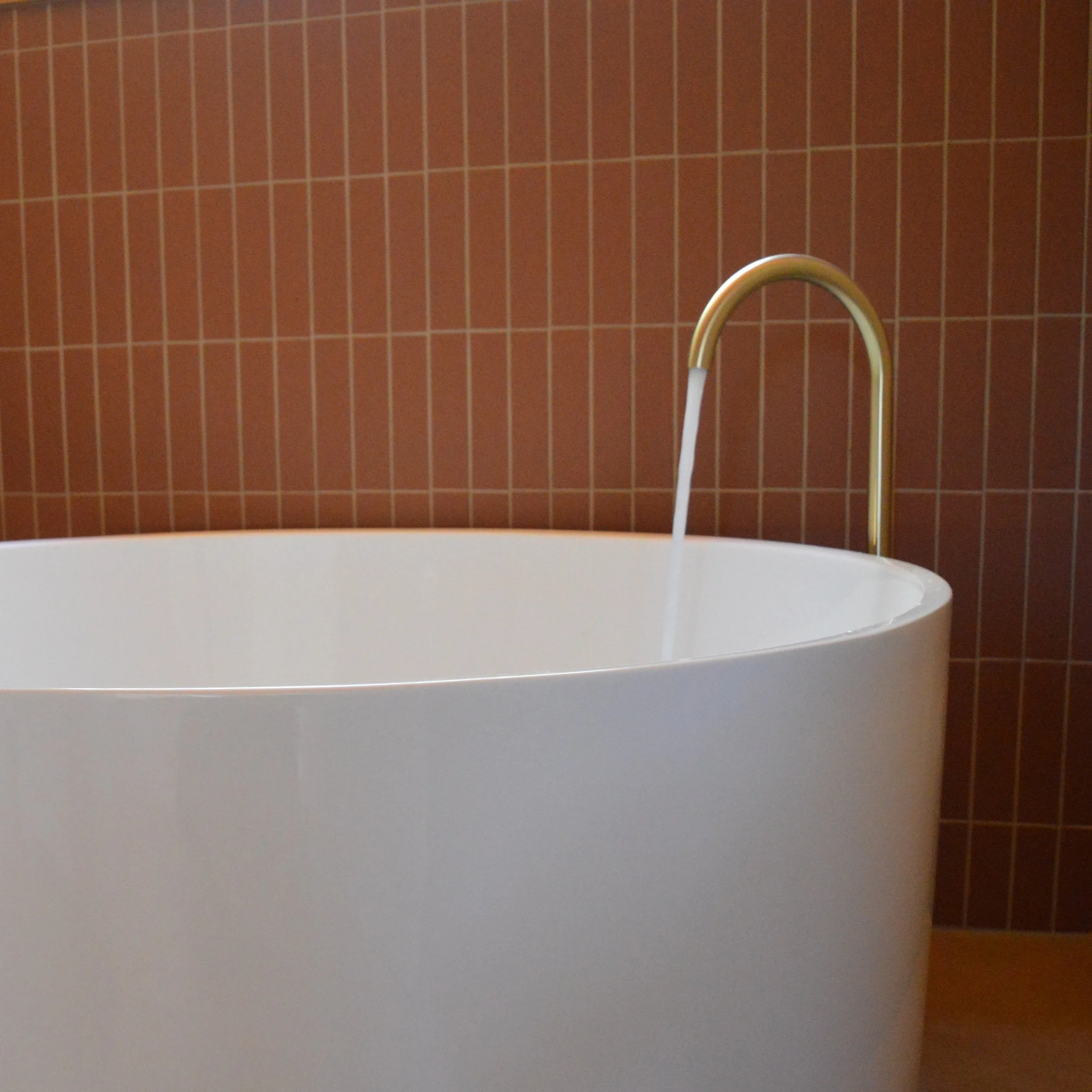 A bathtub with a faucet and water flowing into it, positioned against a brown tiled wall.