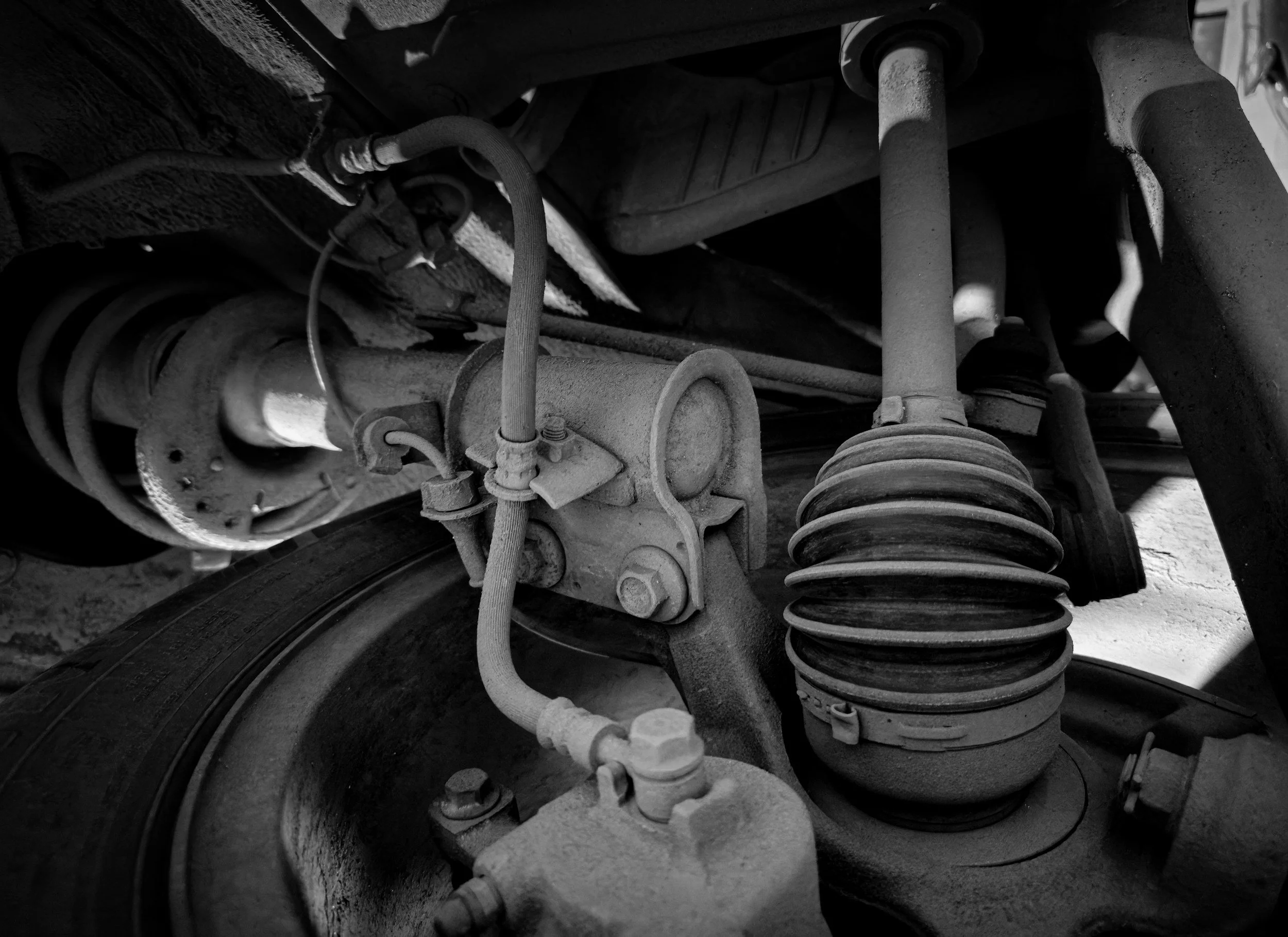 Black and white photo of a vehicle's suspension system showing coil spring, shock absorber, and various connecting parts.