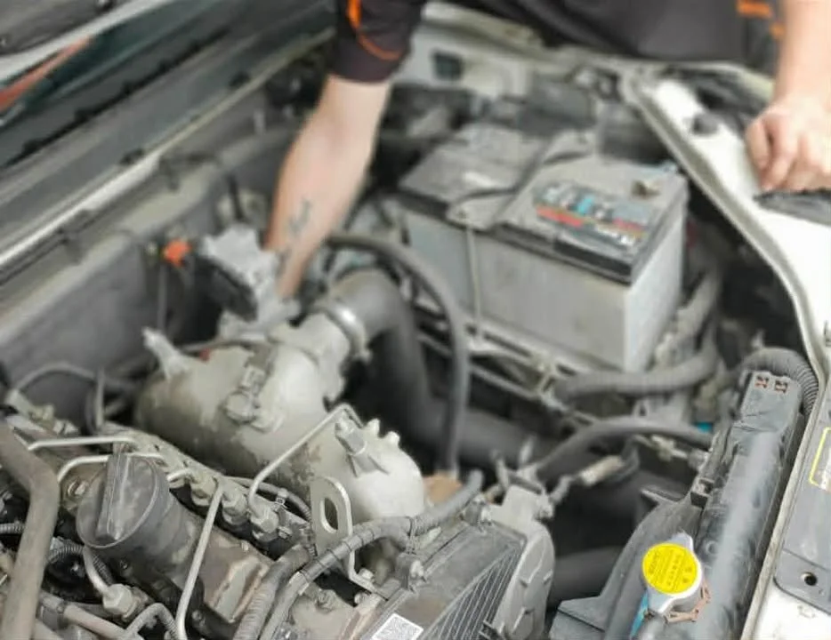 Person working on a car engine with the hood open, inspecting or repairing the engine components.