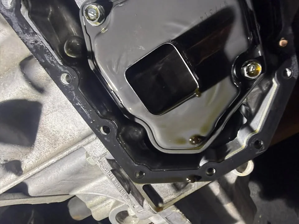 A close-up of an open car transmission with visible oil and parts.