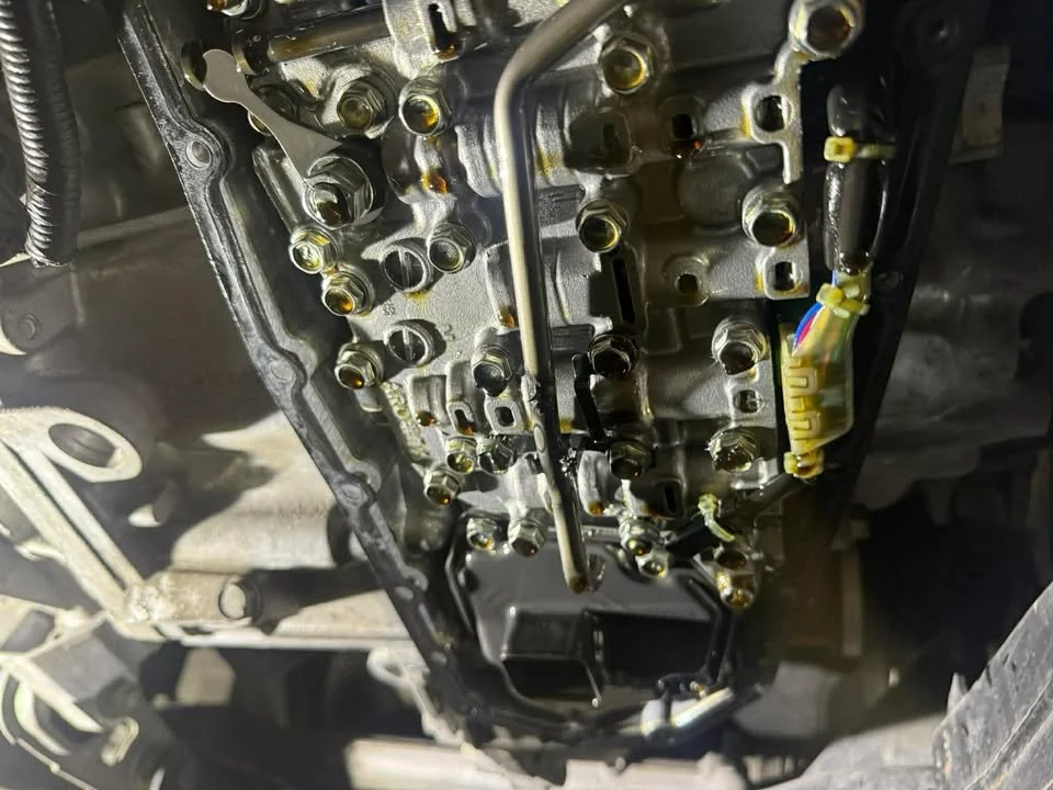 View of a car transmission under the vehicle with bolts and electrical connectors visible