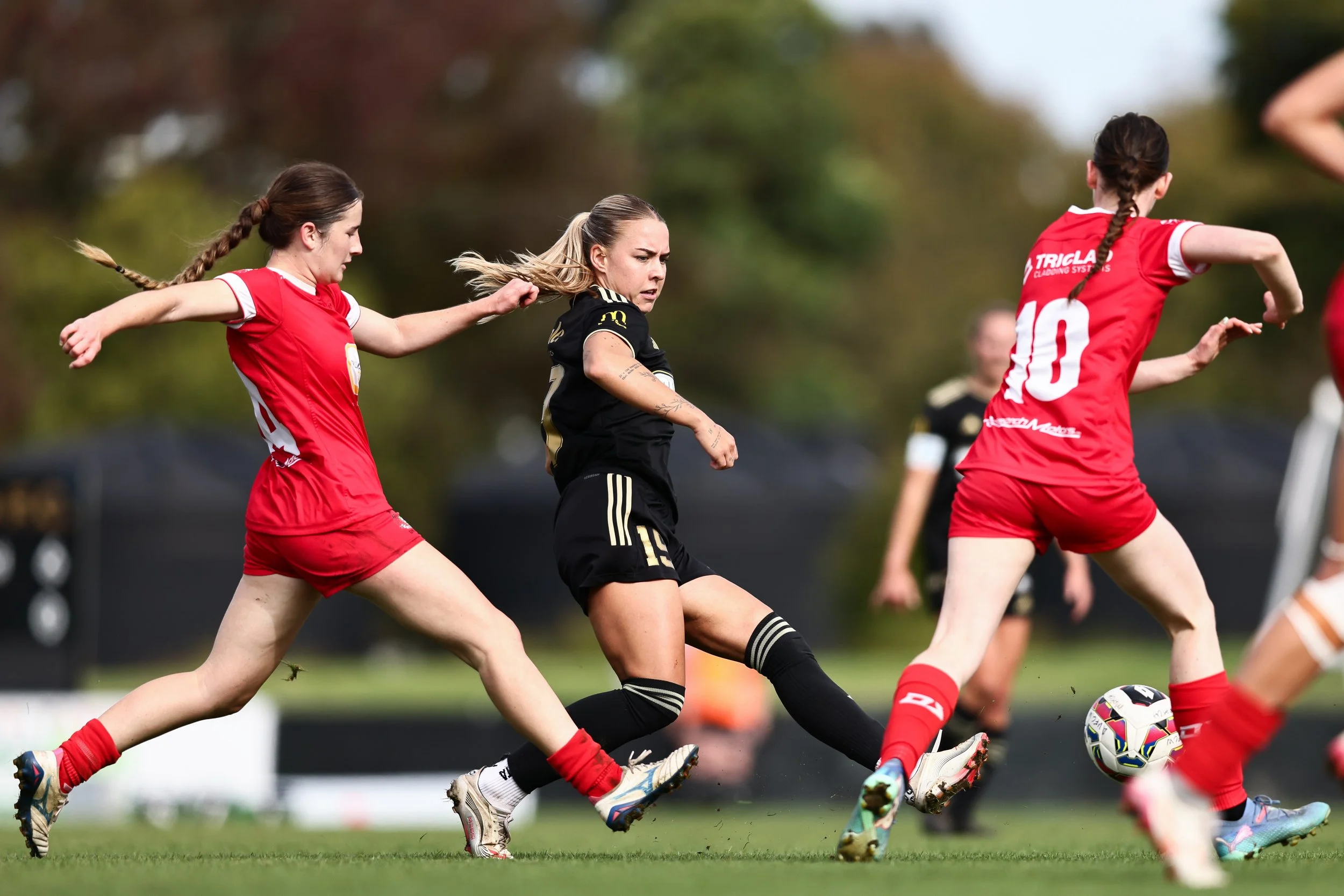 Women playing soccer on a field, running after the ball during a game.
