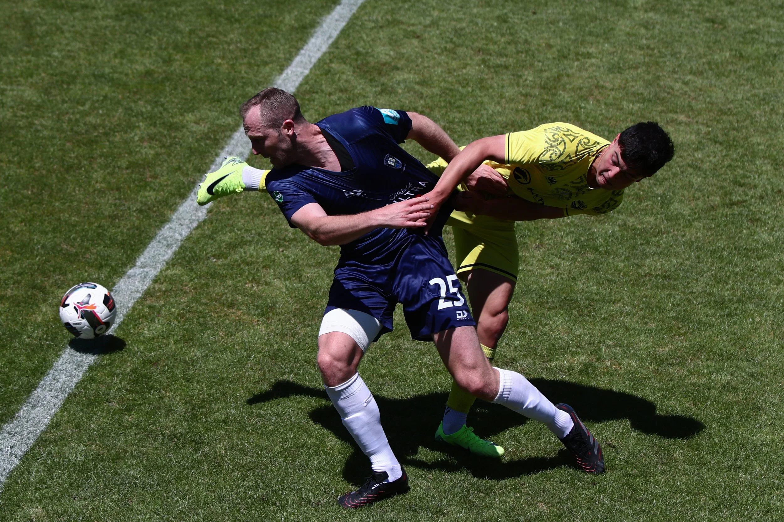 Two soccer players, one in a blue jersey and the other in a yellow jersey, competing for the ball on the field.