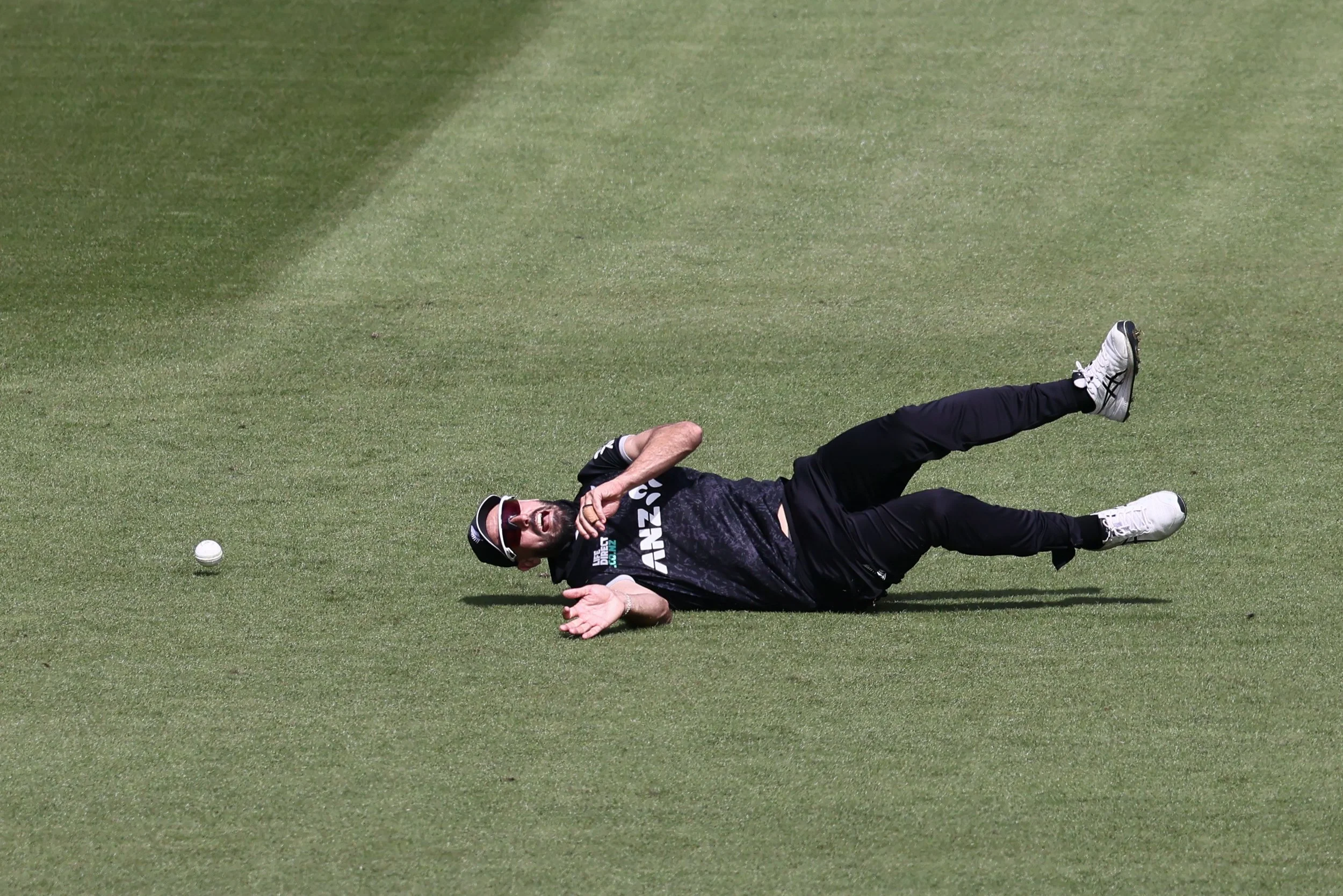 A person lies on a grassy field, wearing black sportswear and white shoes, with a ball nearby.