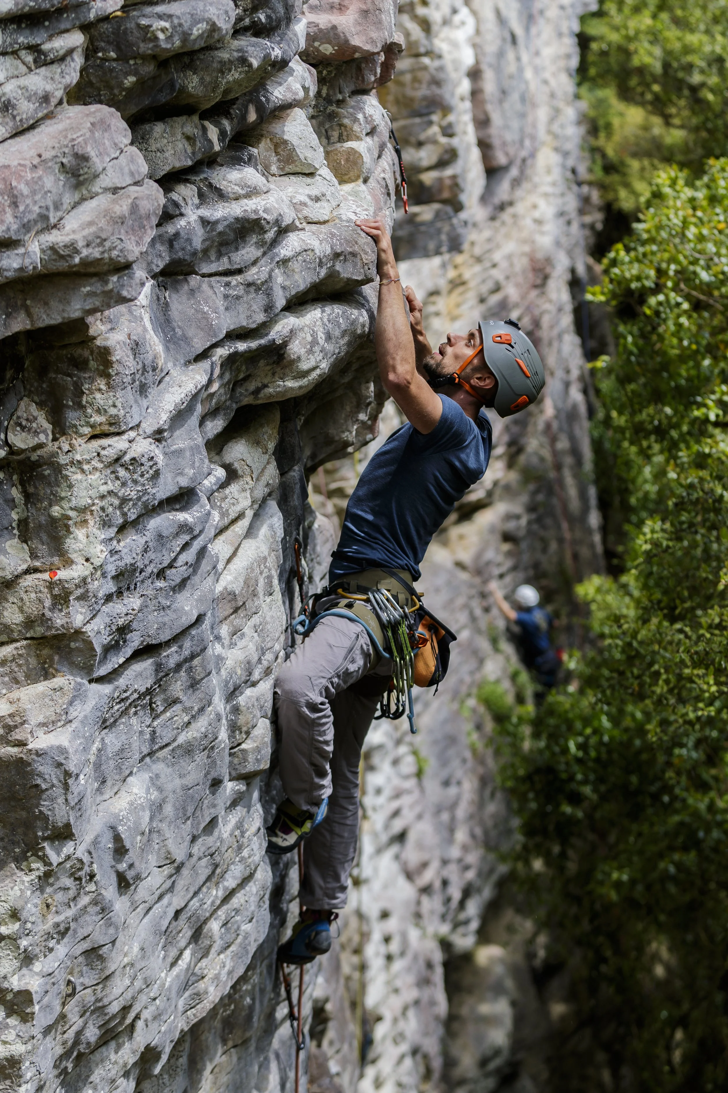 A man rocks climbing on a vertical rock face outdoors, wearing a safety helmet and climbing gear.