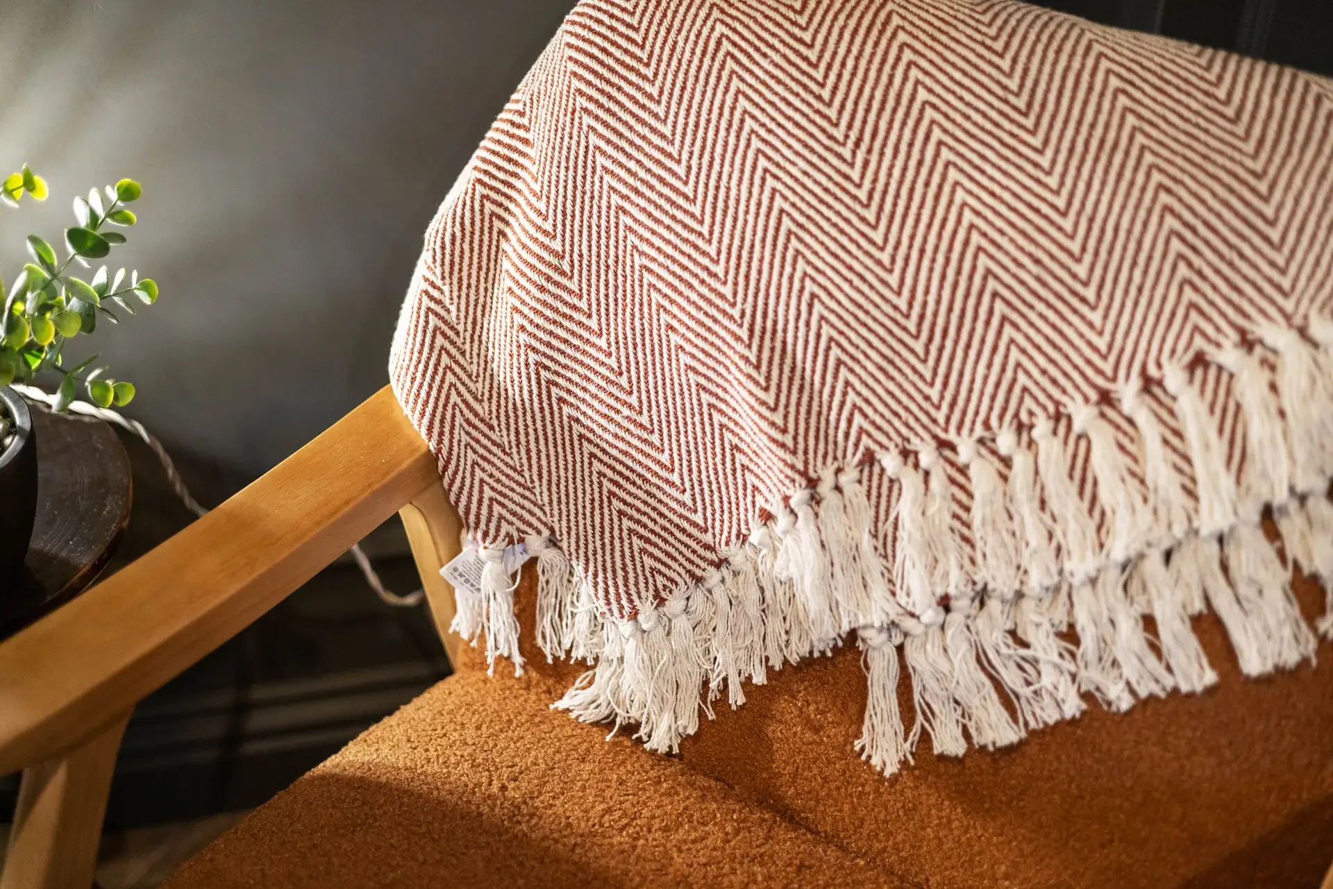 Close-up of a wooden chair with a brown cushioned seat, partially covered by a cream-colored woven throw with red zigzag patterns and fringes, placed on top of the chair.