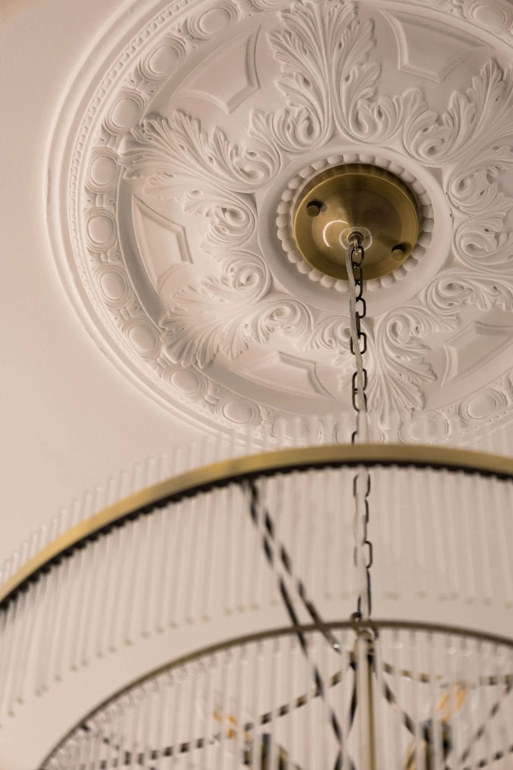 A close-up view of an ornate ceiling medallion with a hanging chandelier chain, showcasing intricate decorative patterns and a brass fixture at the center.