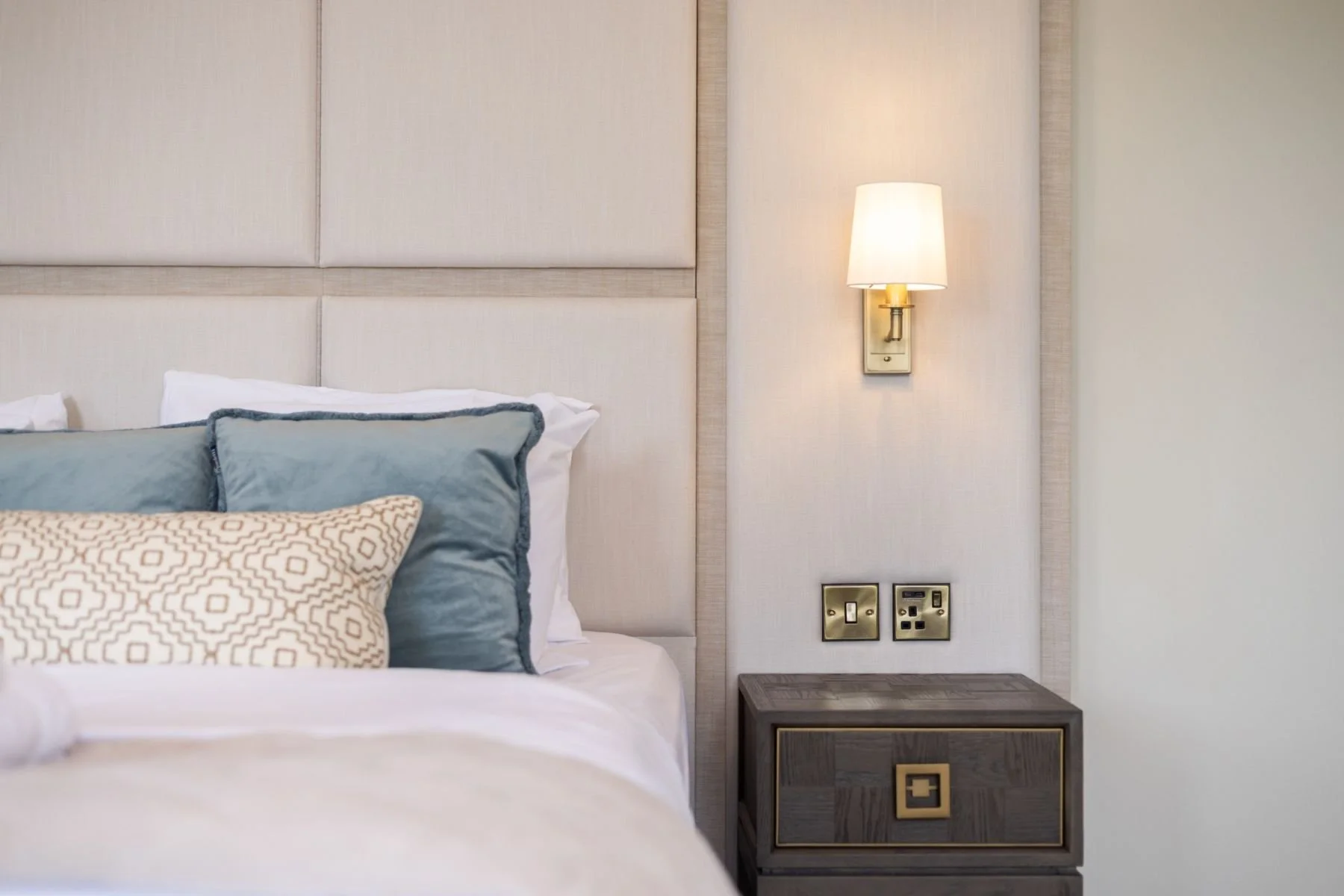 Bedside with upholstered panelled headboard and brass wall light at West Regent Street, Glasgow, by SANNA Design Studio