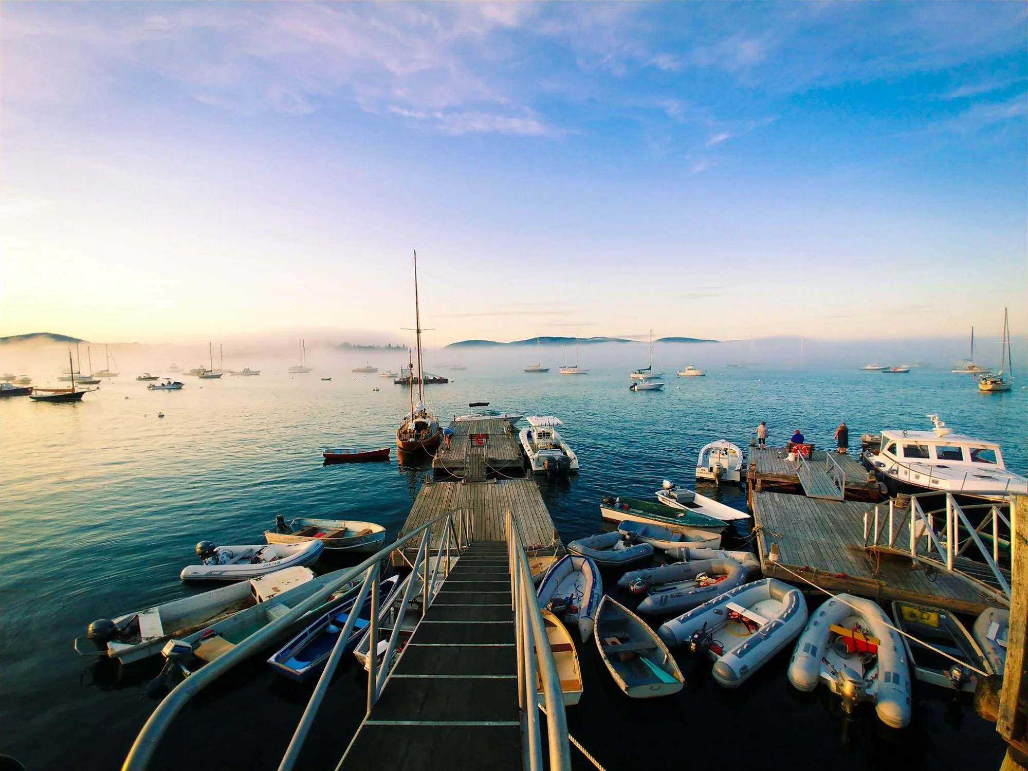 Boats and docks at Manset on Mount Desert Island, Maine, with morning fog lifting over the harbor and islands in the distance.
