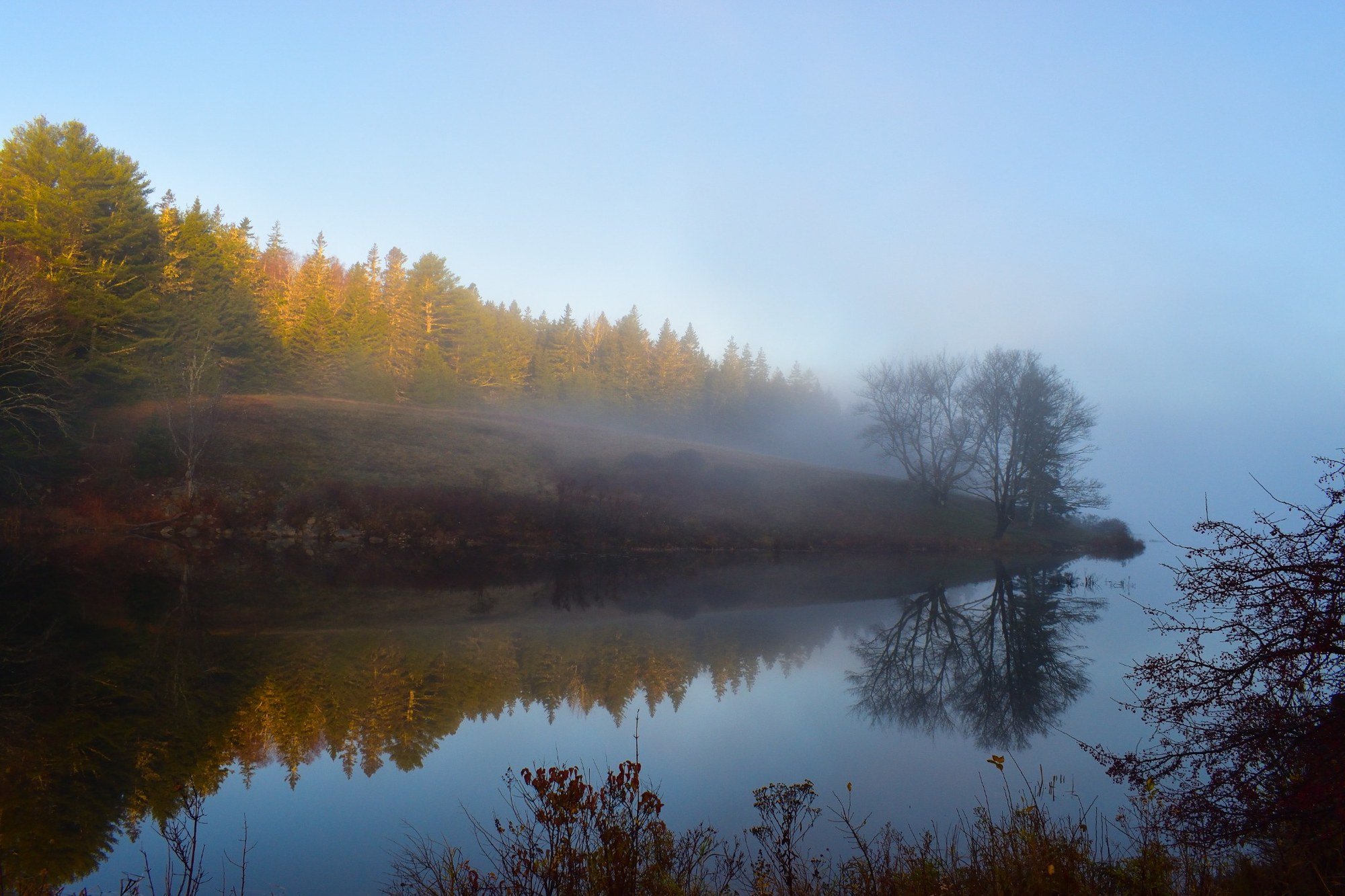 Morning fog drifting over Little Long Pond in Seal Harbor on Mount Desert Island, Maine, with golden trees, still water, and reflections along the shoreline.