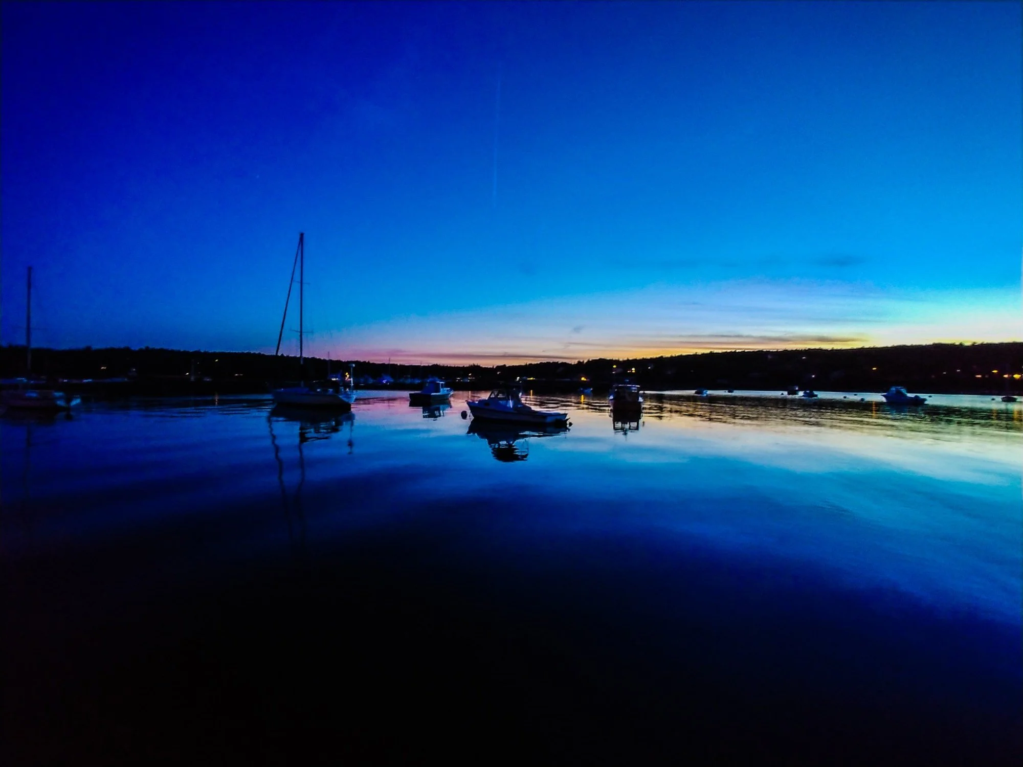 Boats resting on calm water in Southwest Harbor at blue hour, with deep blue reflections and a thin band of sunset on the horizon.