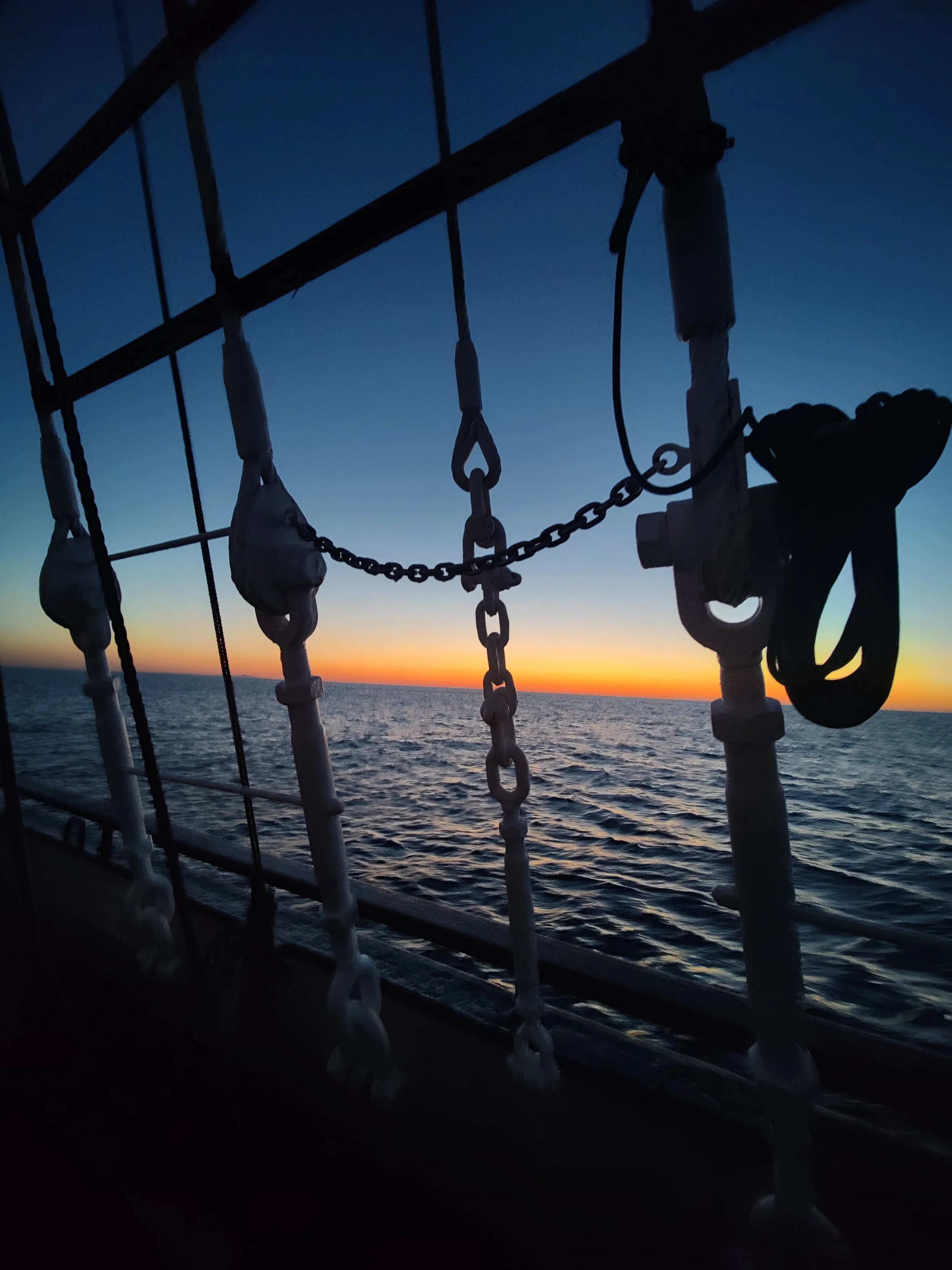 Silhouetted view of a ship's rigging against a vibrant sunset over the ocean