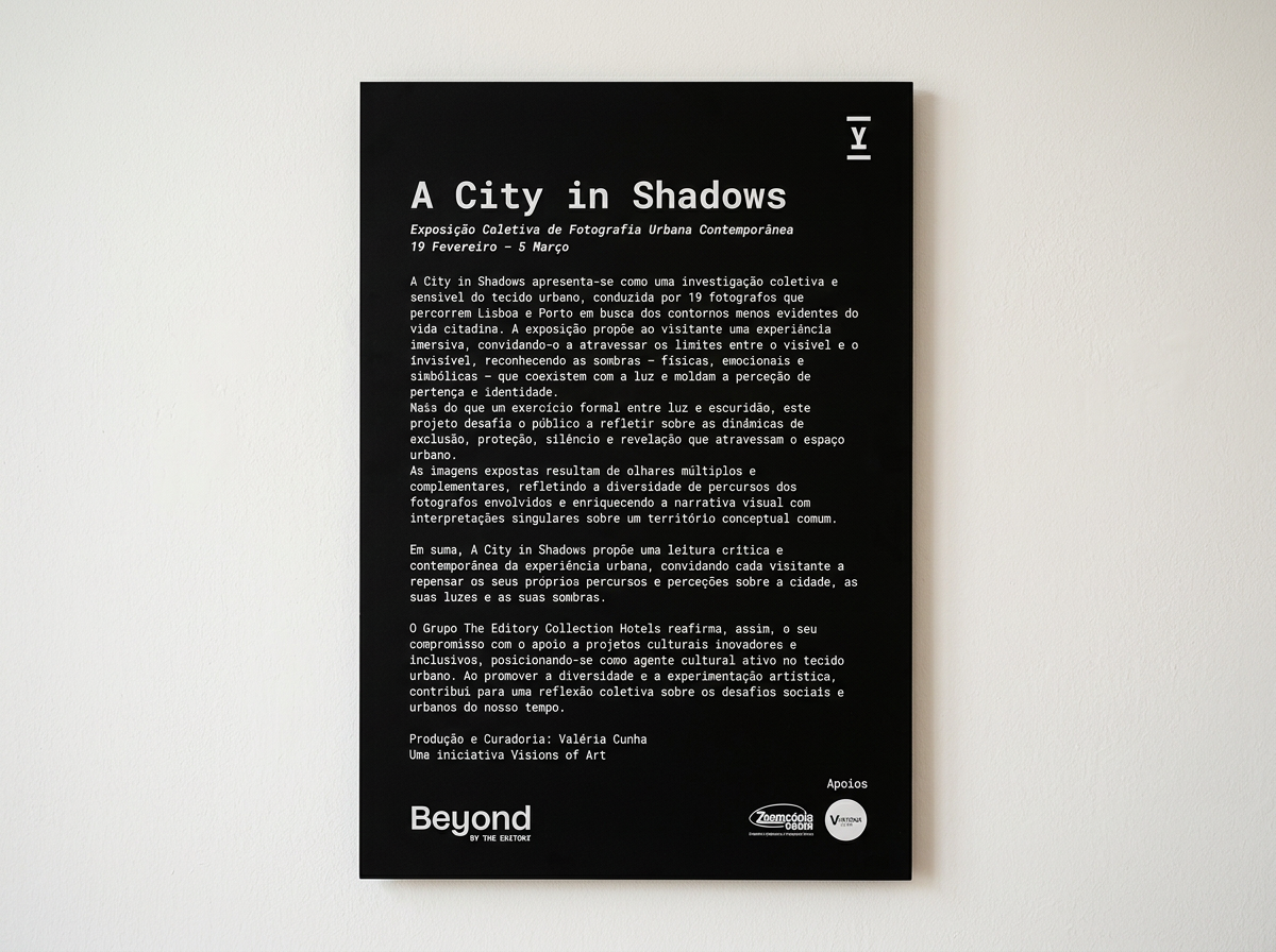 Black exhibition poster with white text titled "A City in Shadows," describing a photography exhibition exploring urban shadows, light, and city perceptions, along with logos of sponsors at the bottom.