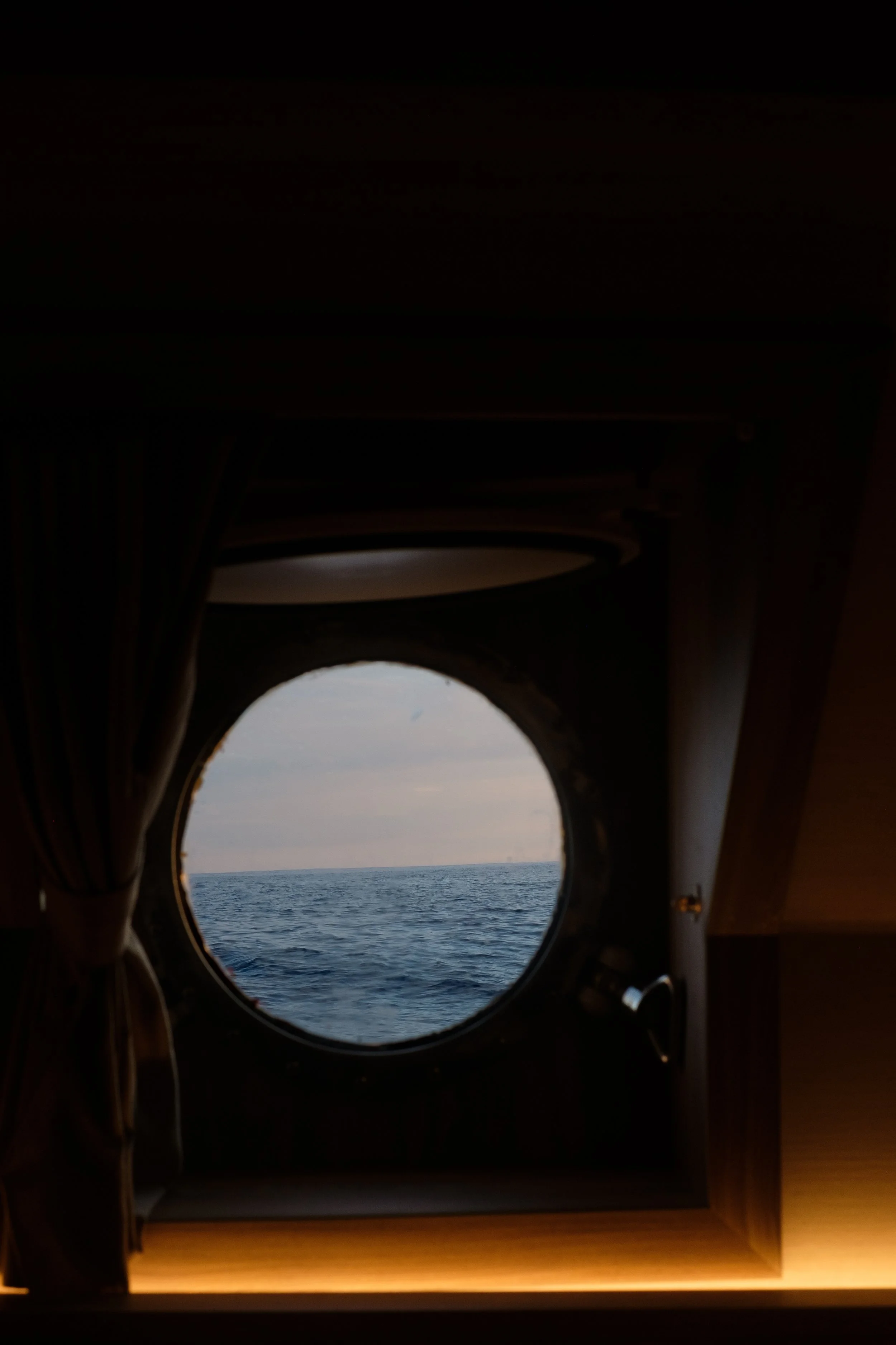 View of the ocean through a porthole on a ship with curtains on the sides.