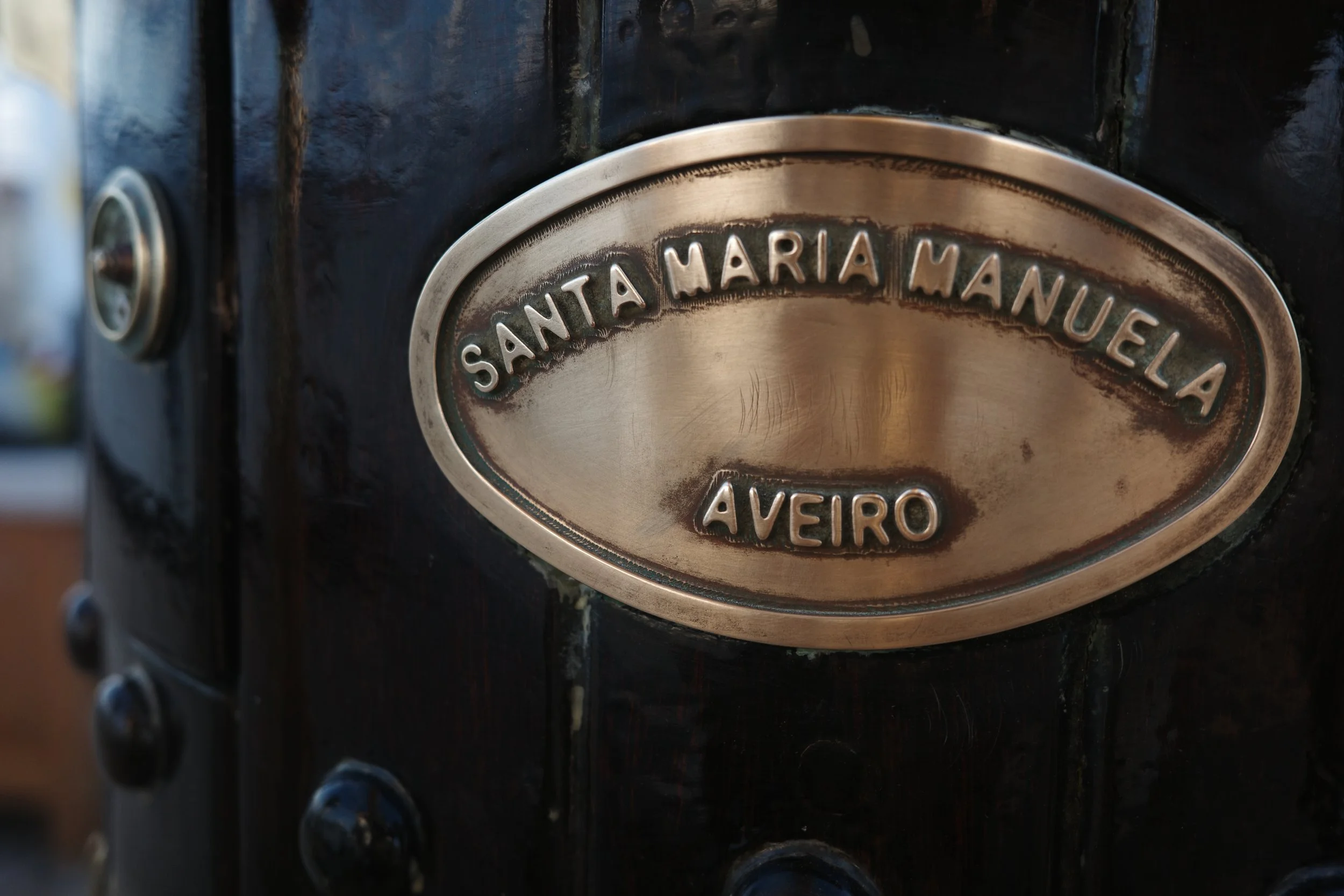 Close-up of a metal plaque with the names Santa Maria Na Nui and Aveiro on a black surface.