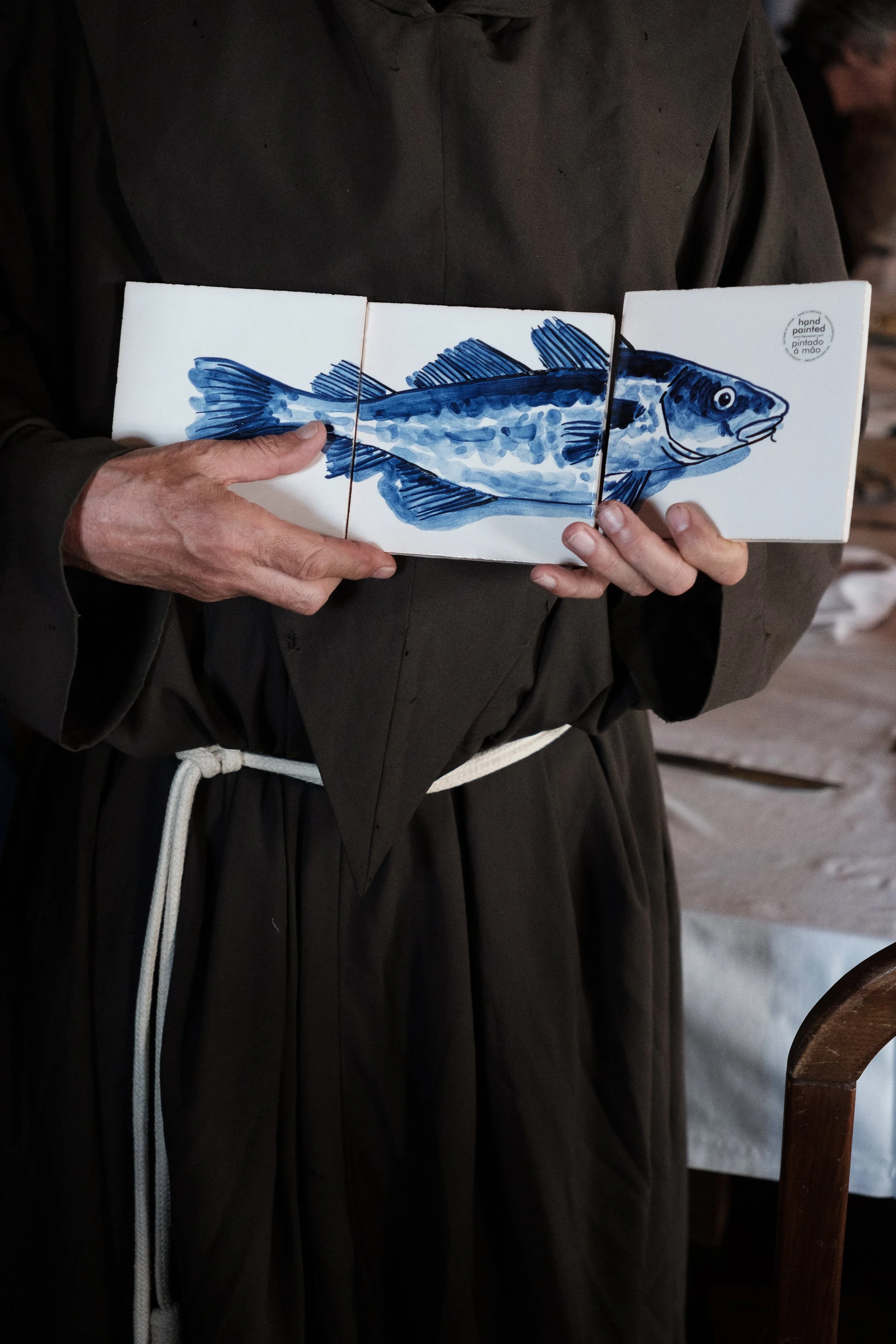 Person holding a white book with a blue fish illustration on the cover, inside a rustic indoor setting.
