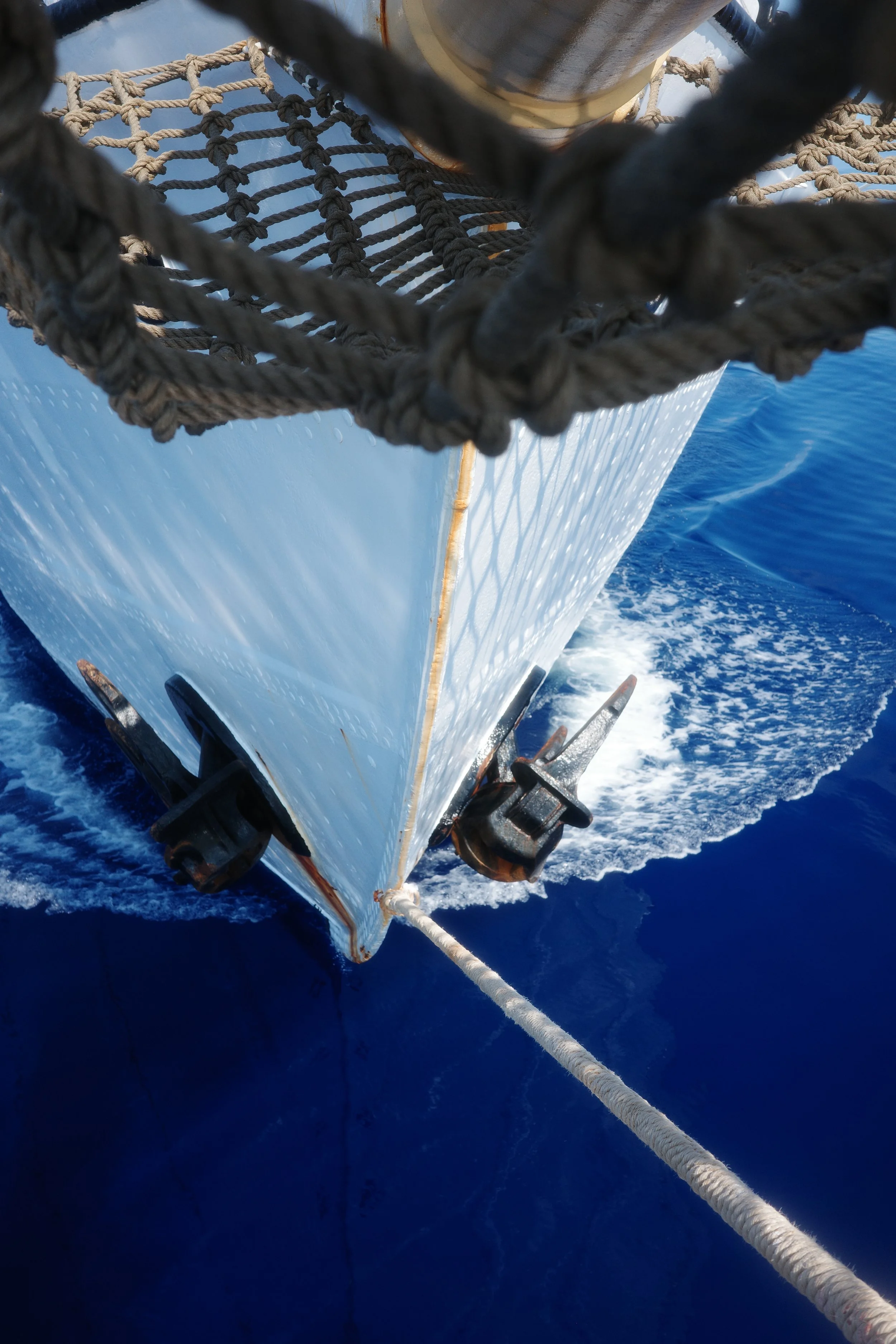 View from the front of a ship looking down at the bow with ropes and rigging, sailing on the open ocean.