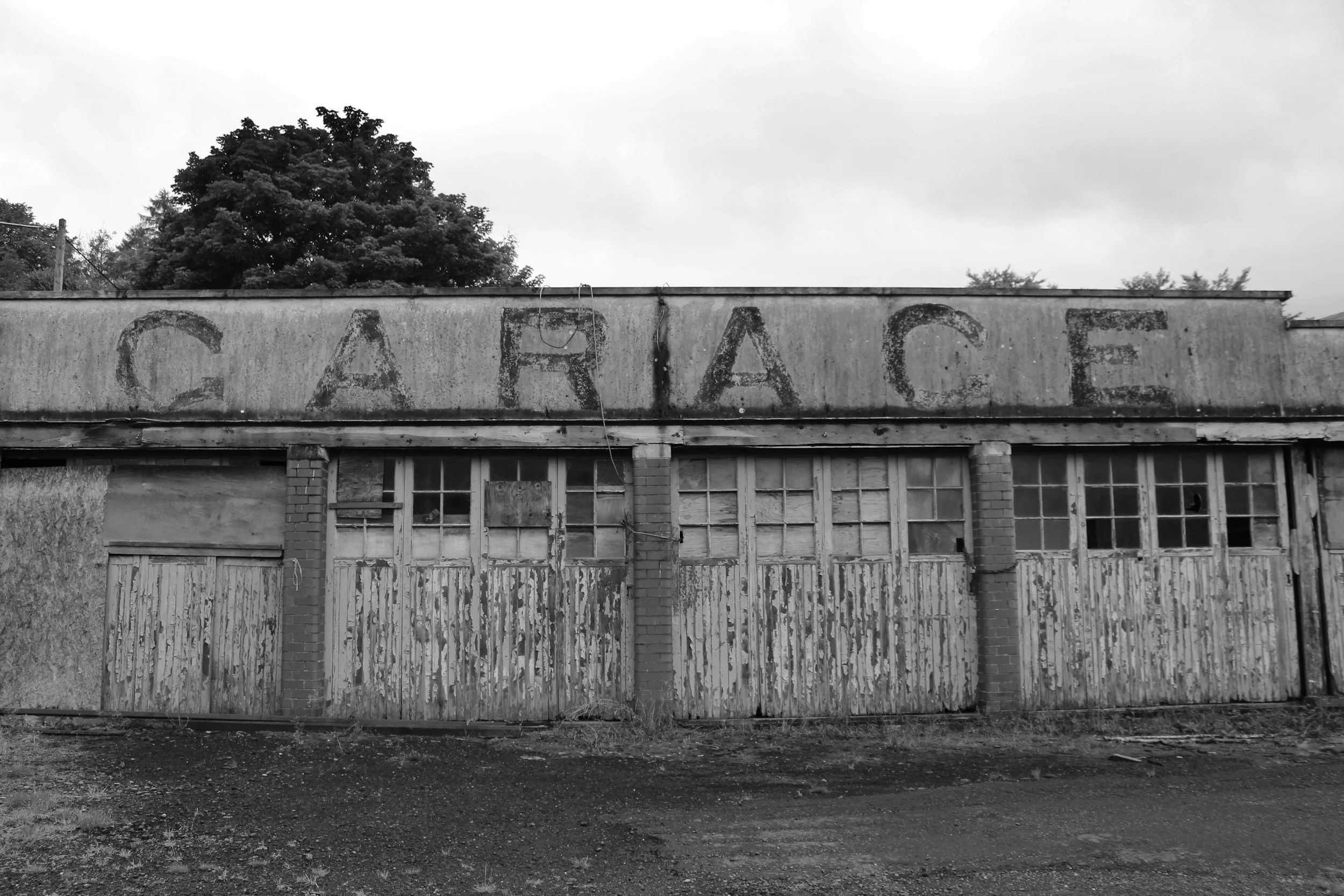 An old, abandoned building with a large, faded sign that reads 'GARBAGE' on the roof, surrounded by overgrown grass and trees in the background.