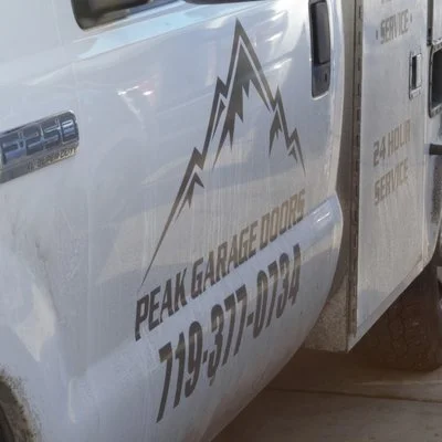 Close-up of a service vehicle door with mountain logo and text for Peak Garage Doors, including phone number 719-377-0734.