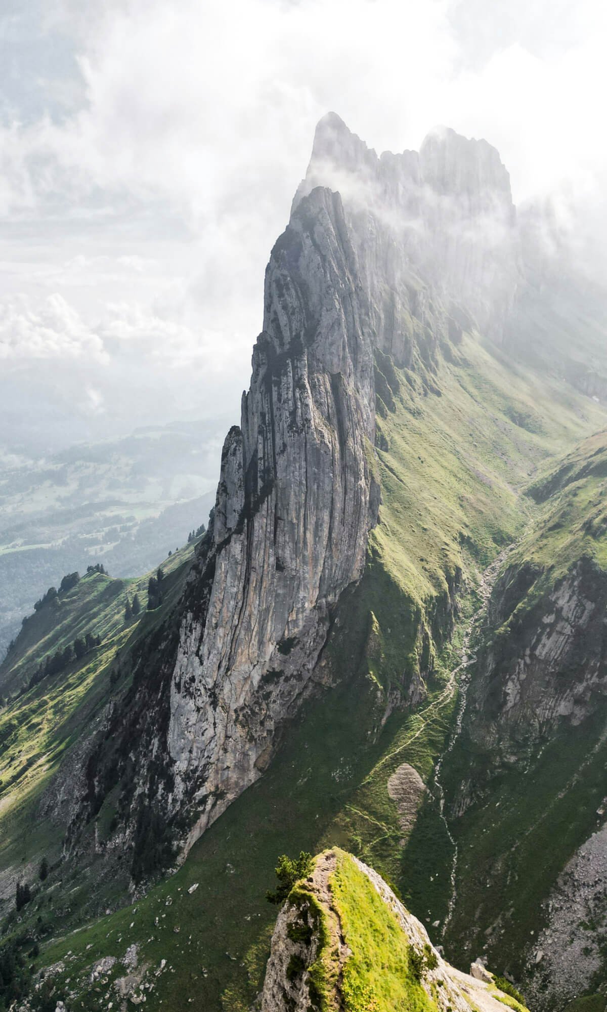 Berggipfel umgeben von Wolken, grüne Hänge und Felsen in den Dolomiten.