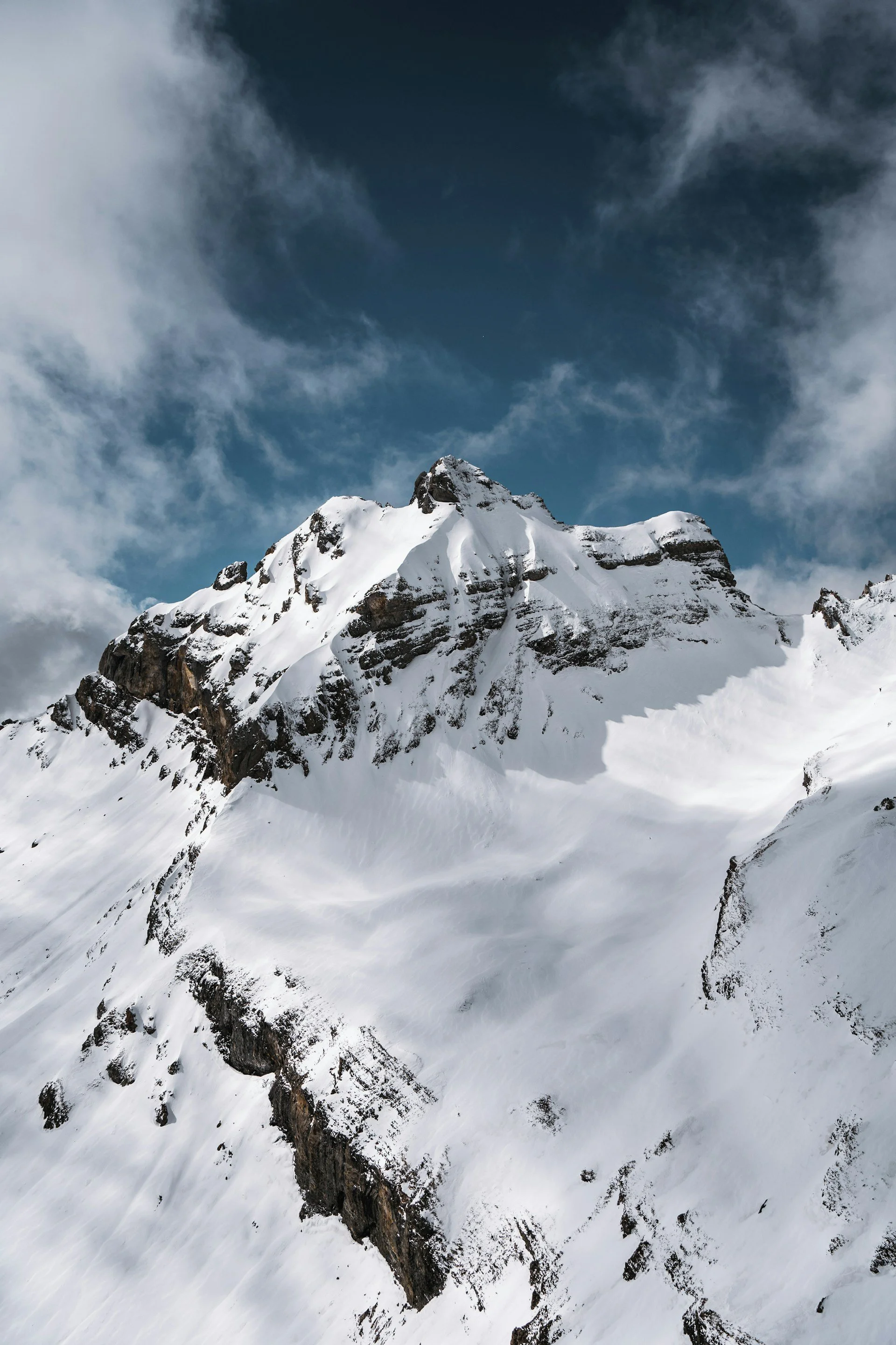 Schneebedeuter Berg mit schroffen Felsen und Wolken im Himmel