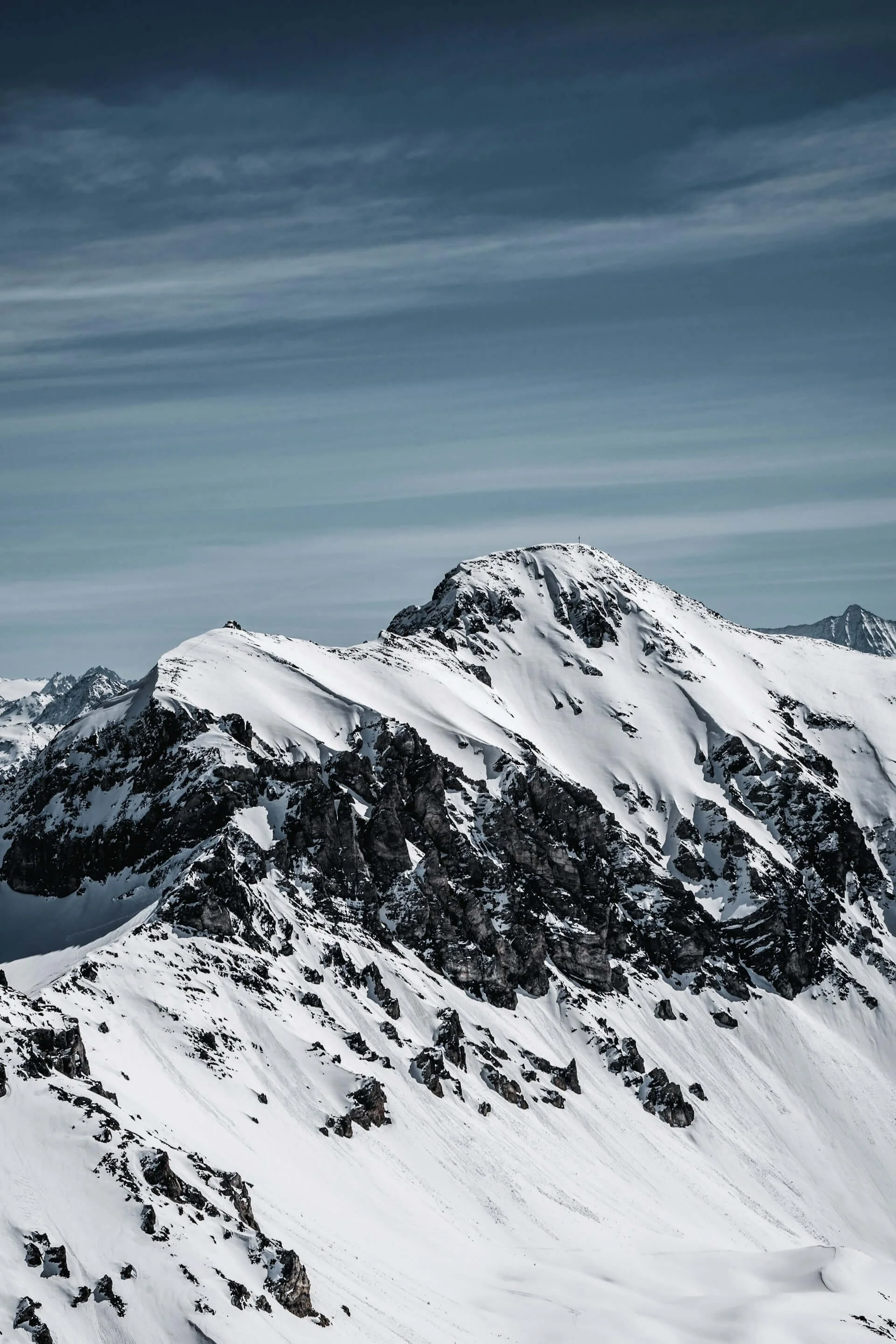 Schneebedeckte Berggipfel unter einem bewölkten Himmel in einer hohen Gebirgsregion.