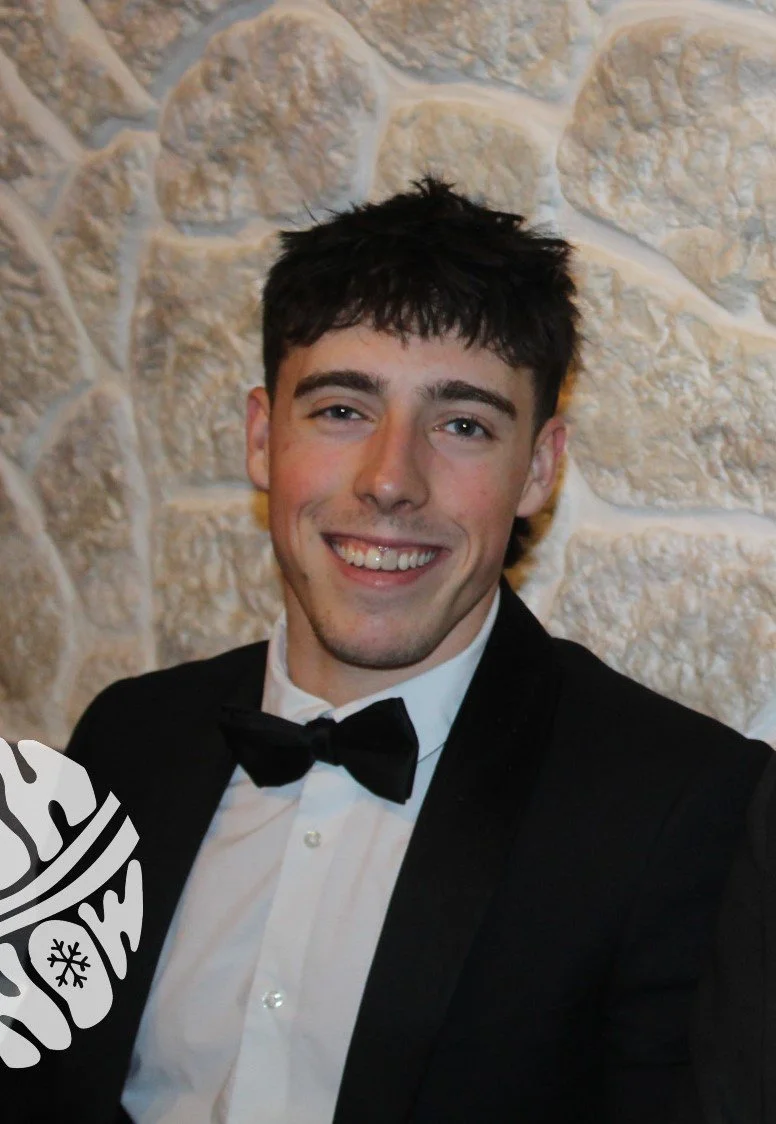 Young man smiling in formal attire against a stone wall background.