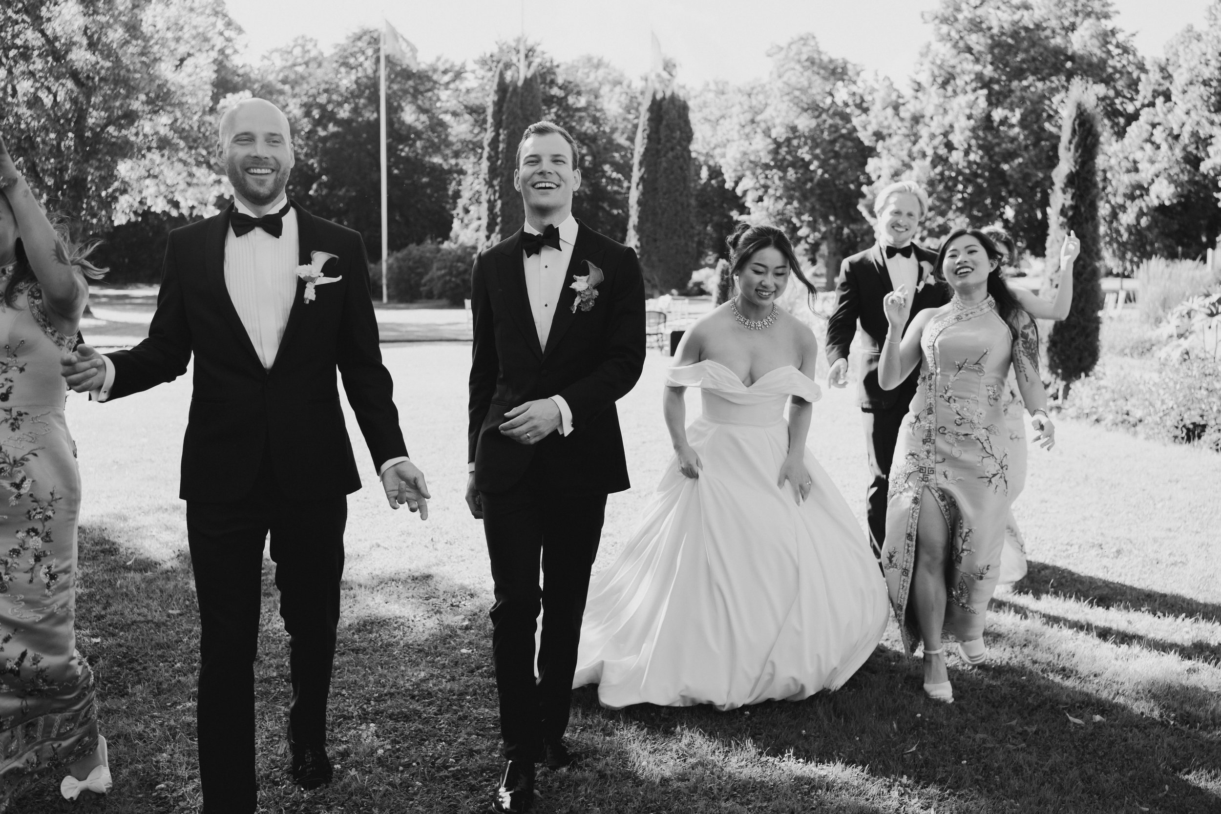 A group of people dressed in formal attire, walking outdoors in a park during daytime, smiling and enjoying the event.