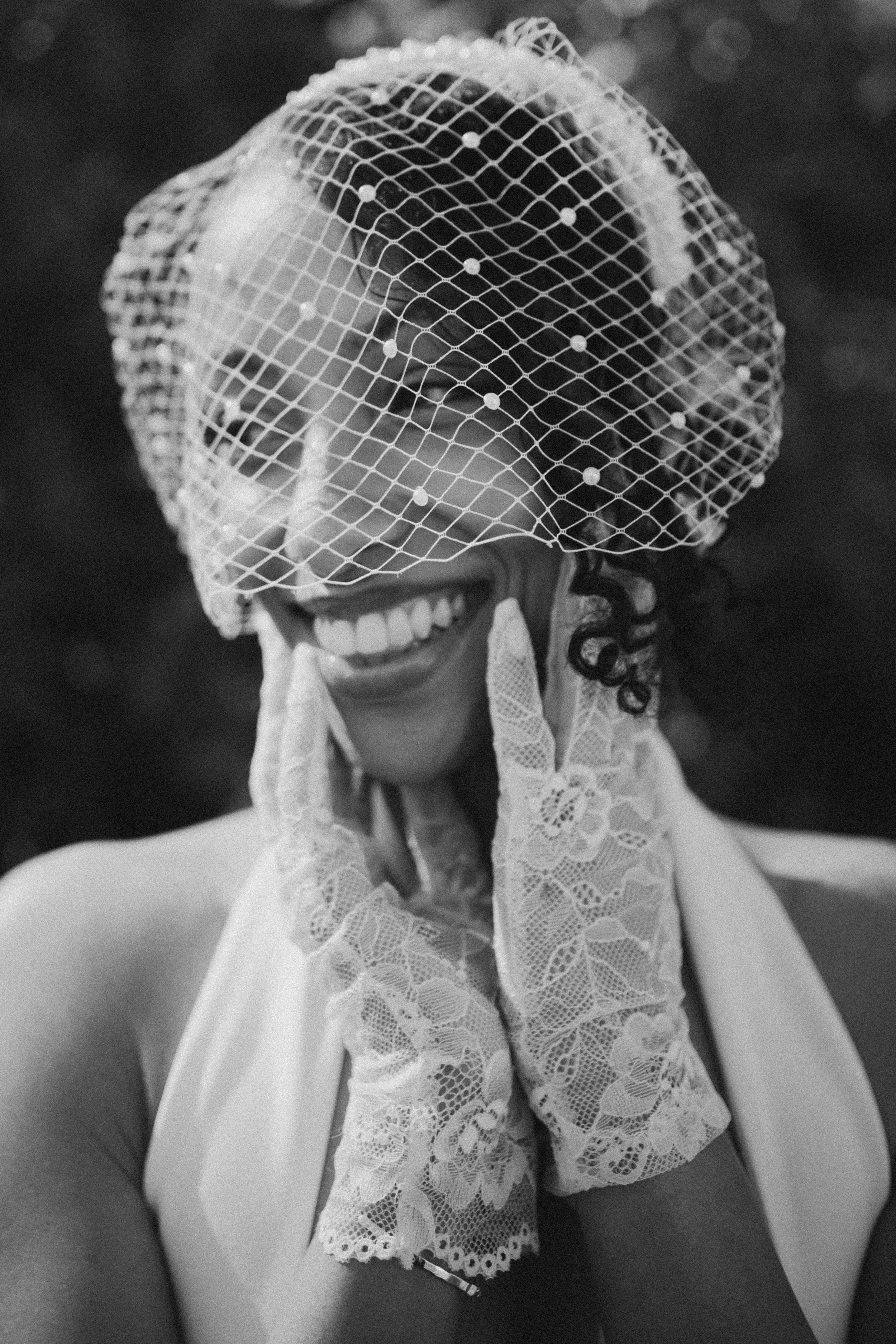 A woman wearing lace gloves and a lace dress with a veil dancing or smiling at a celebration or wedding event.