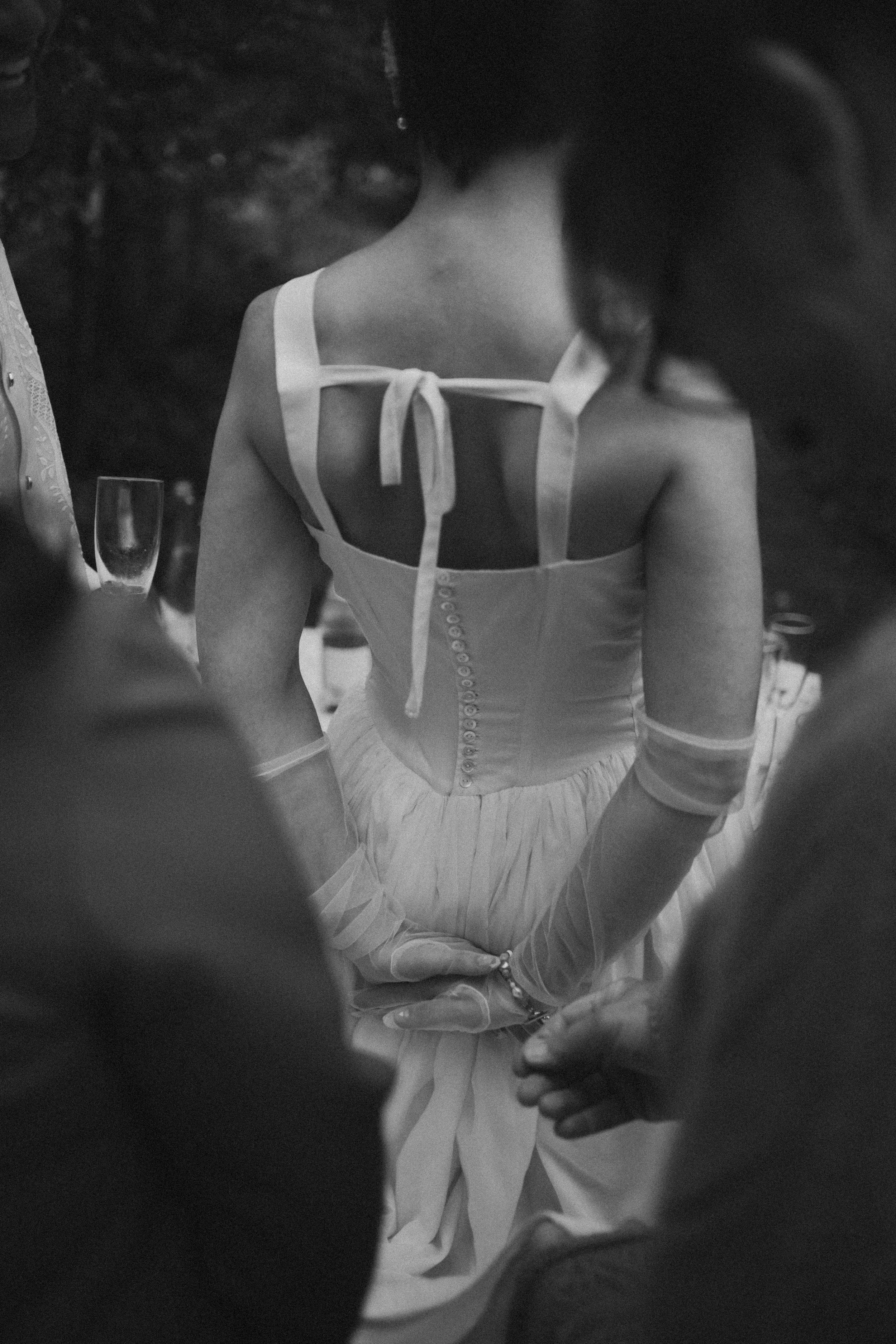 A woman in a light-colored dress with a bow on the front, holding someone's hand in a dance or social gathering setting.