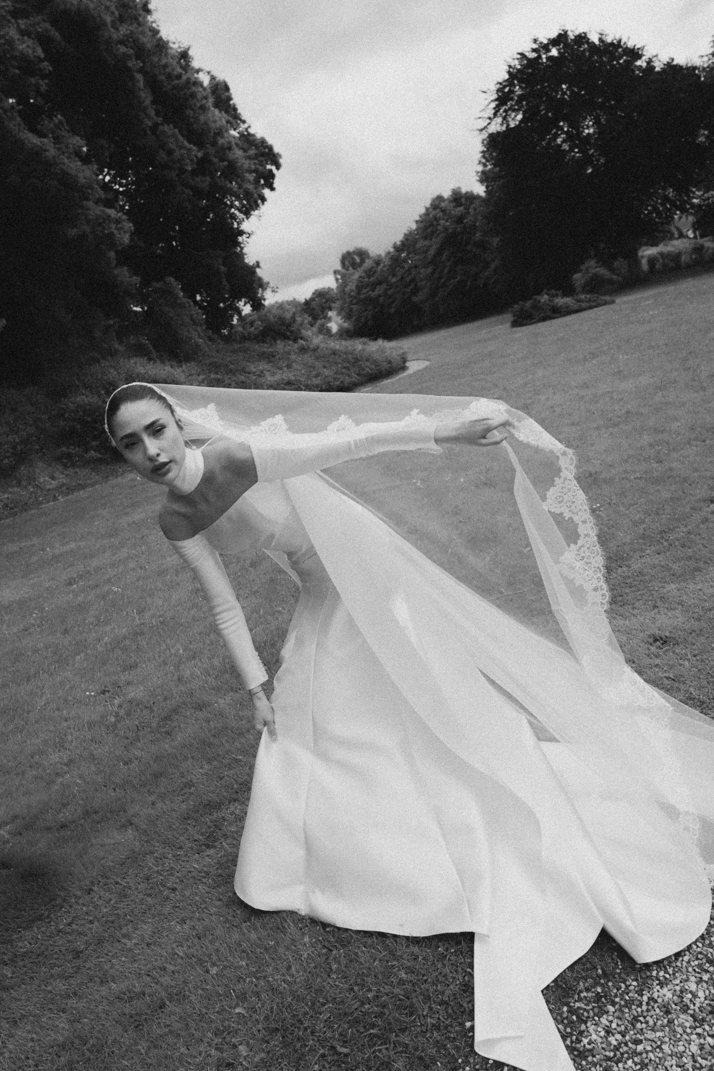 Woman in wedding dress lying on the grass outdoors with trees in the background.